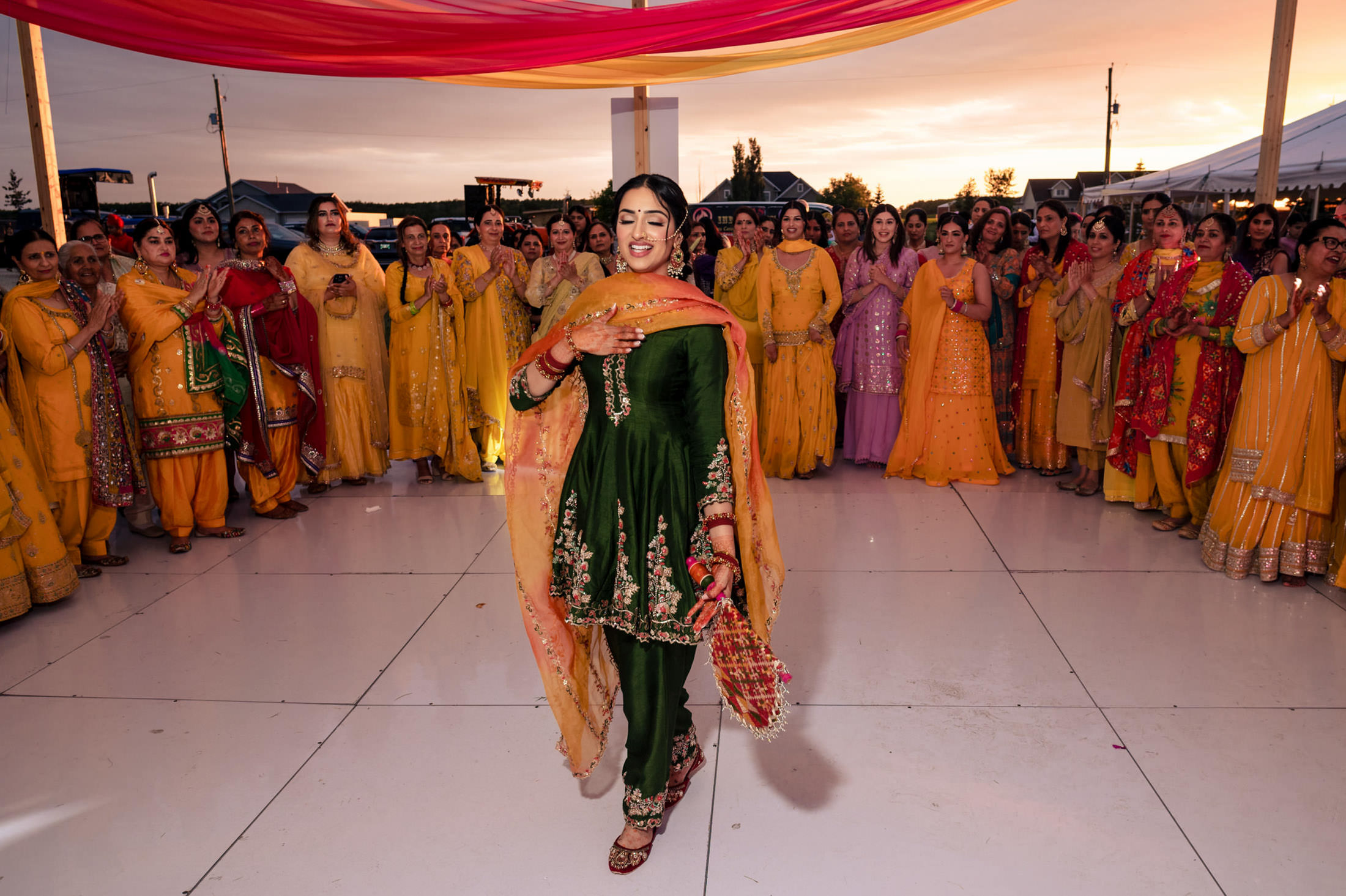 Woman in green dancing at Winnipeg wedding, surrounded by women in colorful traditional attire.