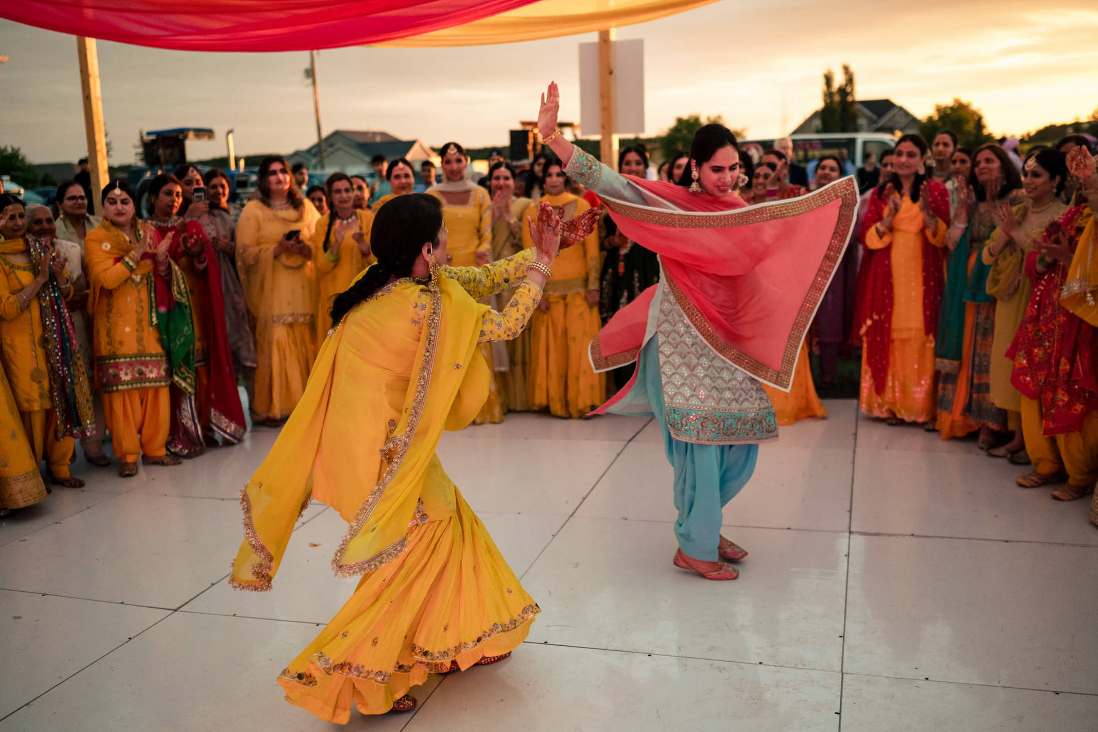 Two women in vibrant attire dance joyfully at sunset, like a Winnipeg wedding celebration.