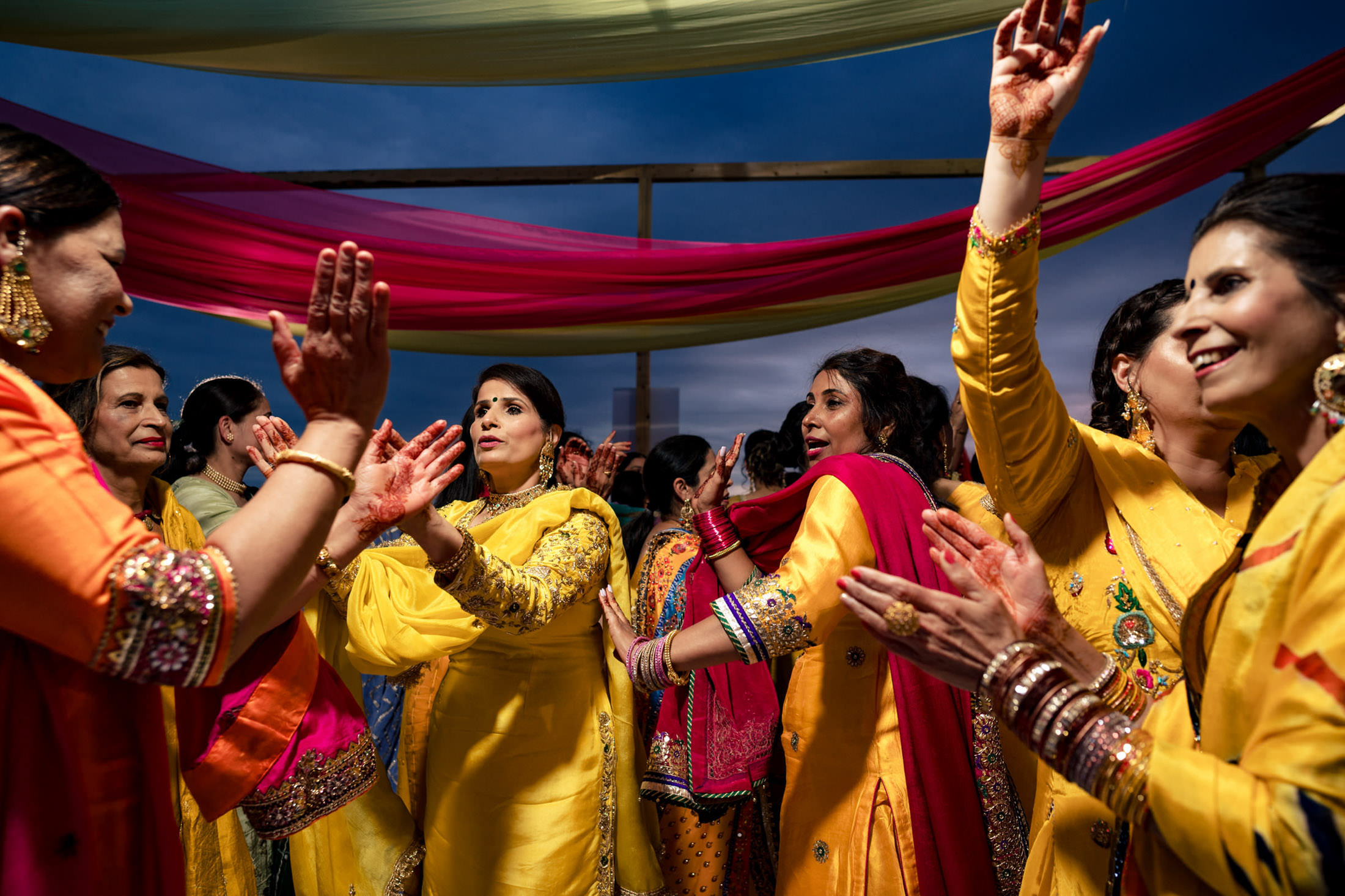 People dancing and celebrating a Winnipeg wedding under colorful drapes in vibrant attire.