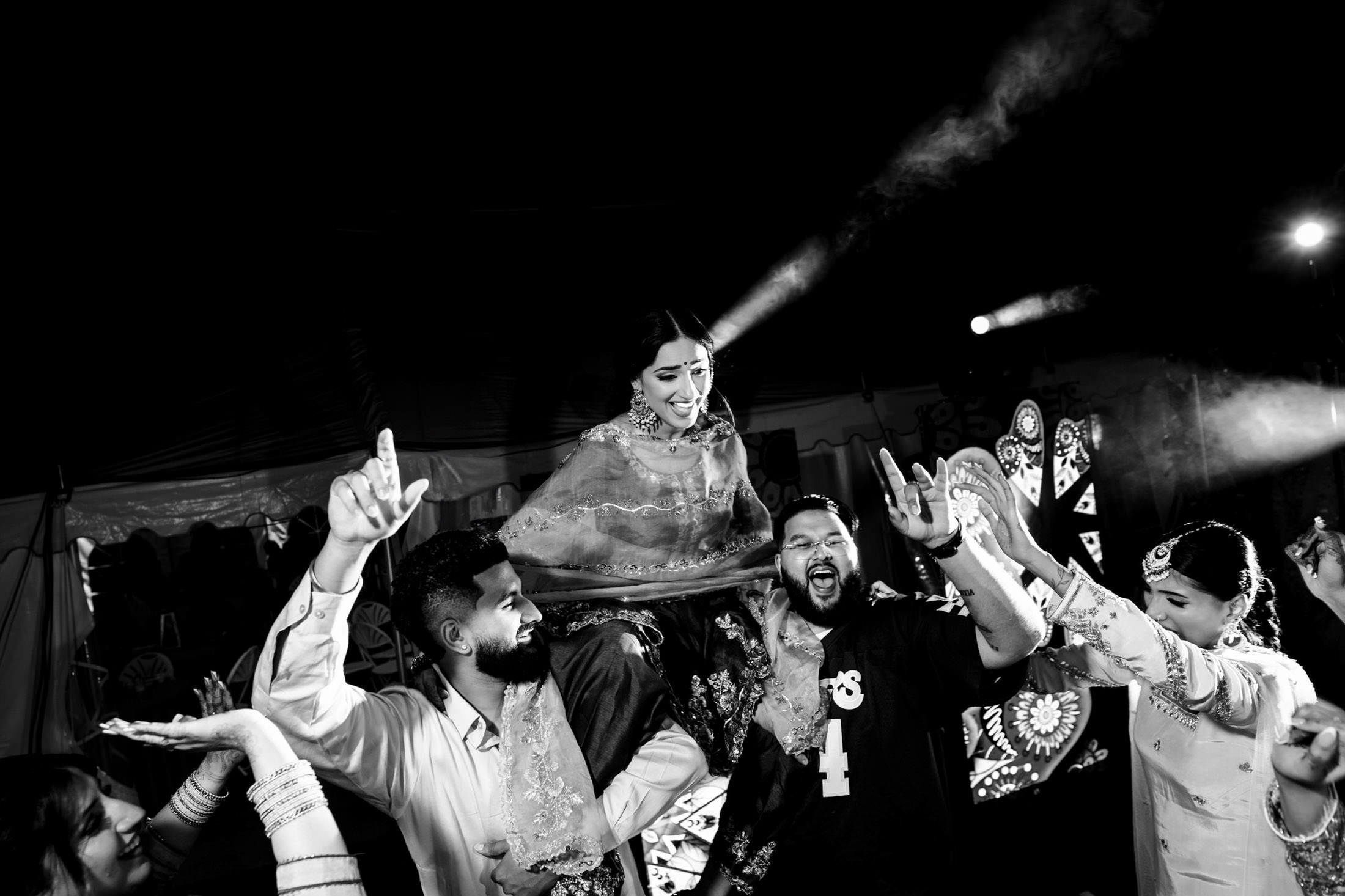Bride dancing joyfully on shoulders at a lively Winnipeg wedding, surrounded by cheering crowd.