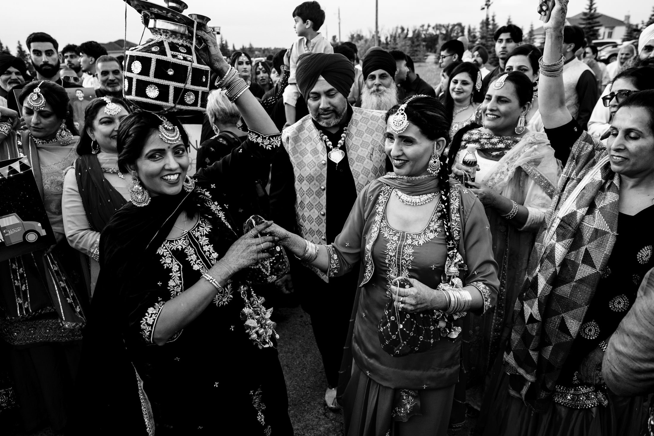 People celebrating at an outdoor Winnipeg wedding, some in traditional attire, smiling and dancing.