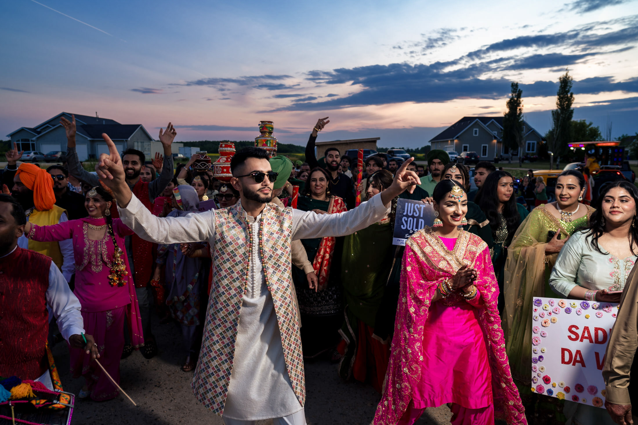 A Winnipeg wedding group celebrates outdoors in colorful traditional attire at sunset.