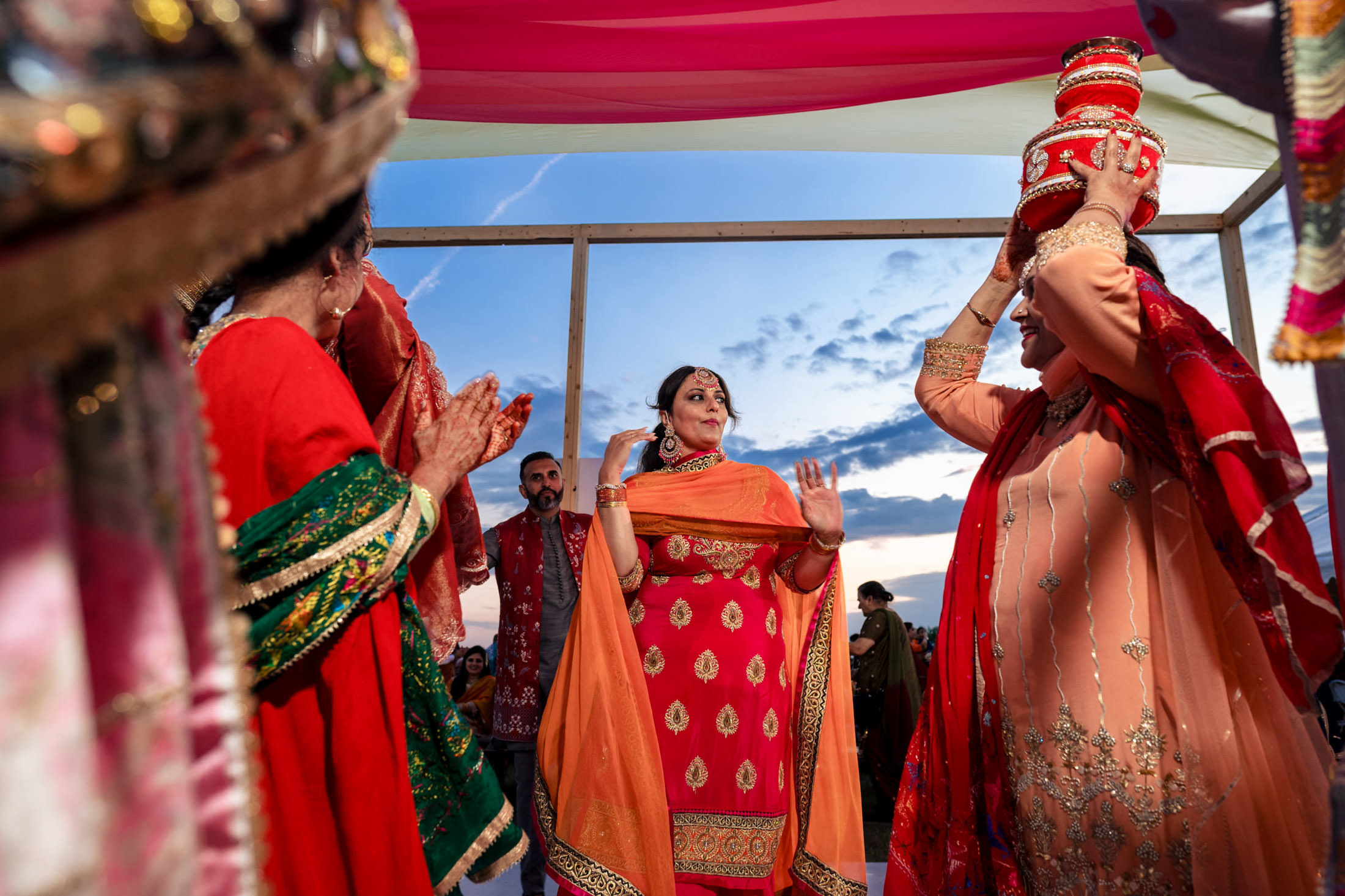 Women in vibrant attire celebrate a Winnipeg wedding with dance under a colorful canopy.