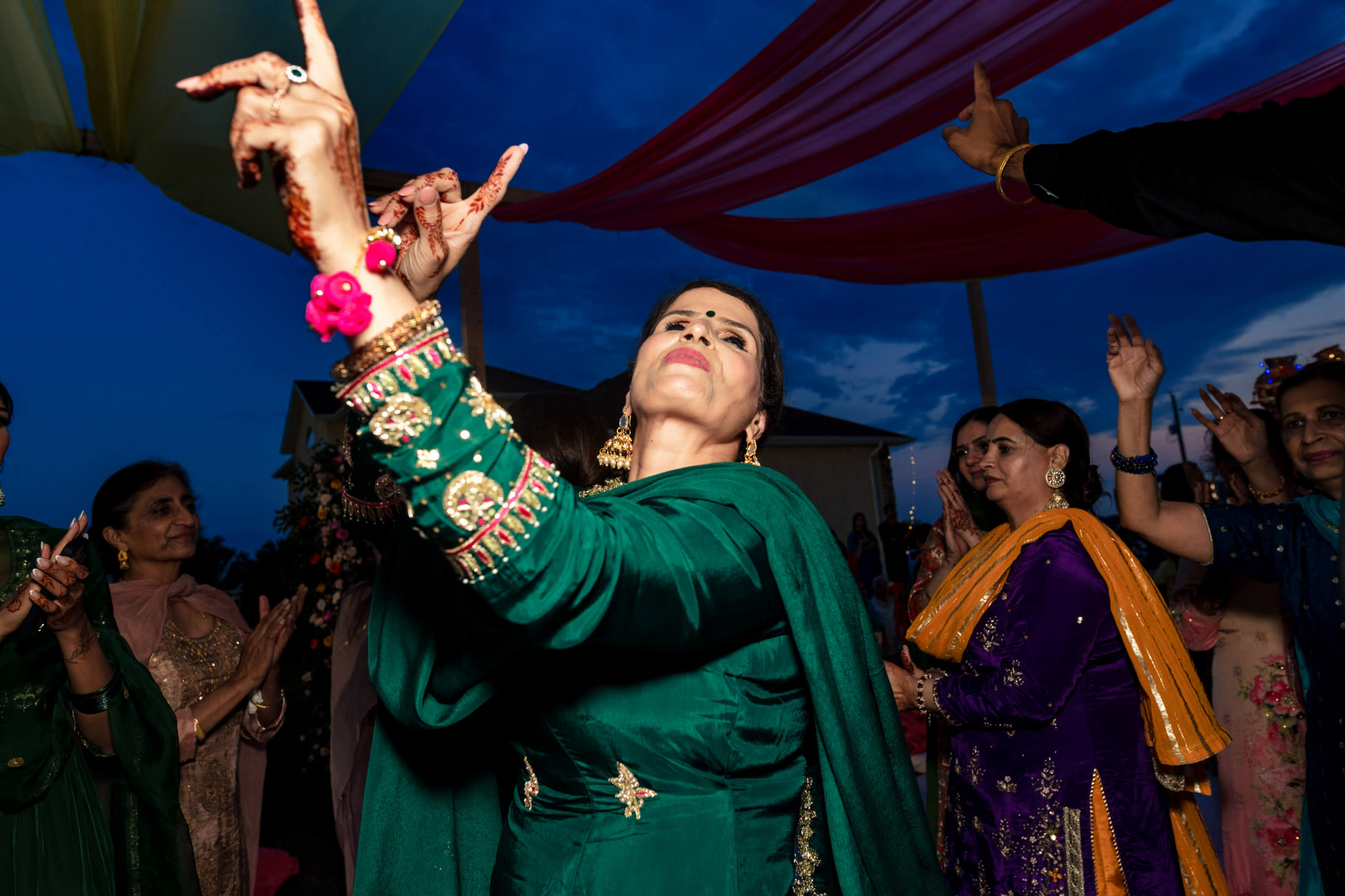 Person in green dancing at an outdoor Winnipeg wedding, arms raised, among colorful guests.
