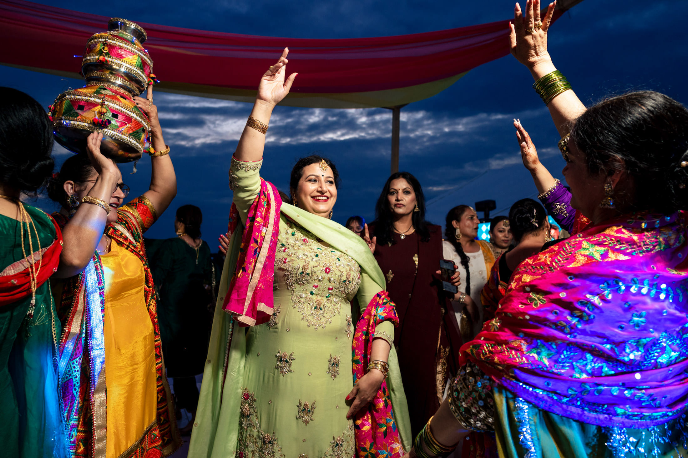 Winnipeg wedding guests dance energetically in vibrant traditional attire under a colorful canopy.