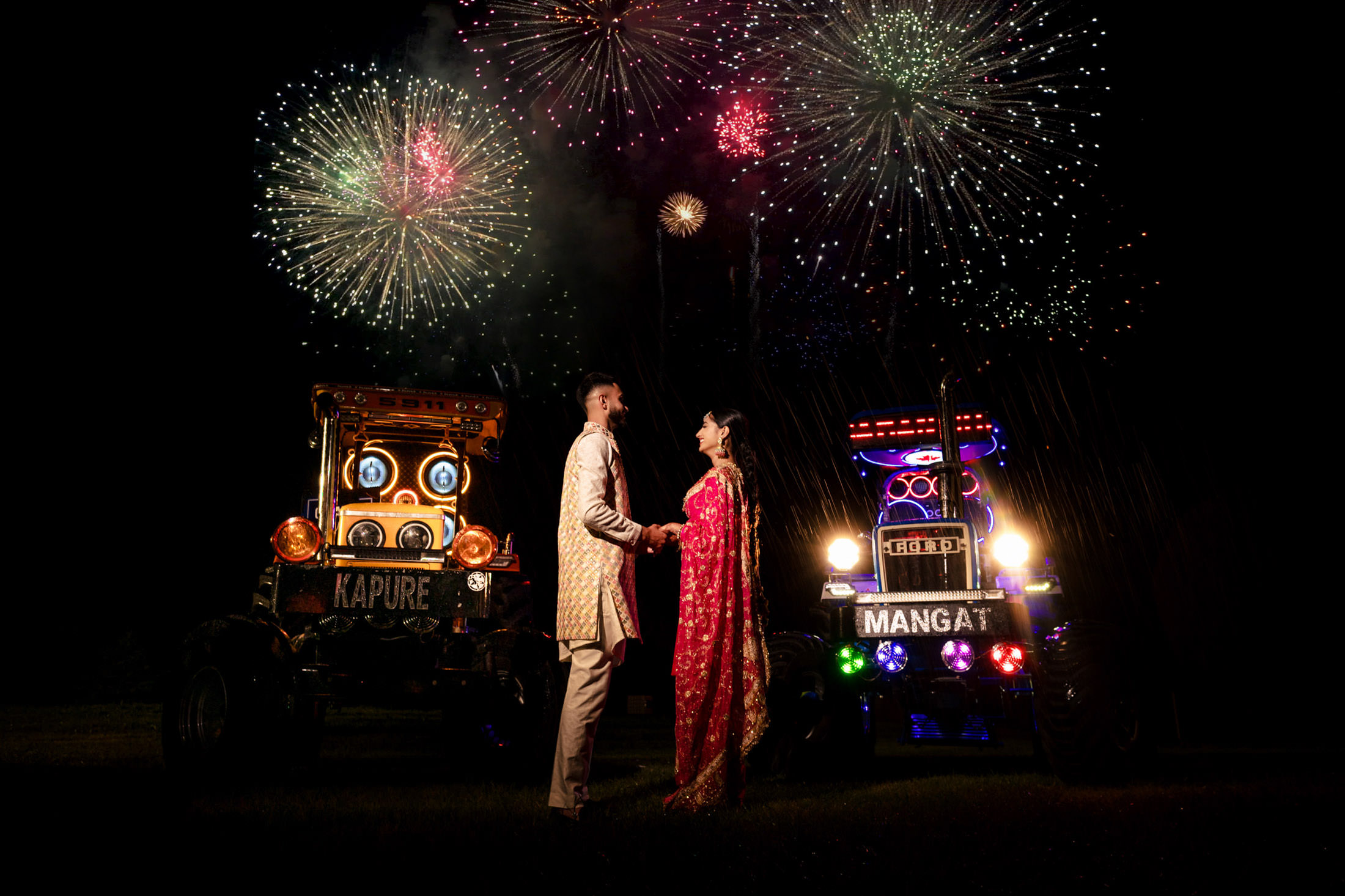 A couple in traditional attire holds hands at a Winnipeg wedding with tractors and fireworks.