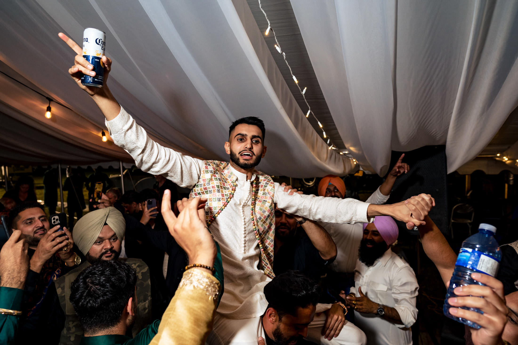 Man celebrating at a lively Winnipeg wedding, holding a drink, surrounded by cheering crowd.
