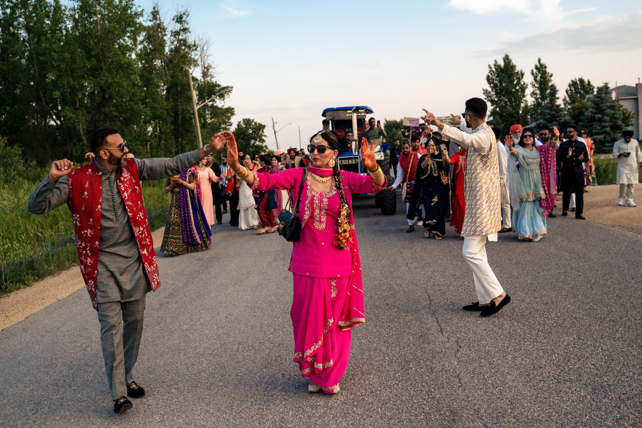 Dancing joyfully in traditional attire on a Winnipeg wedding road, with a tractor behind.