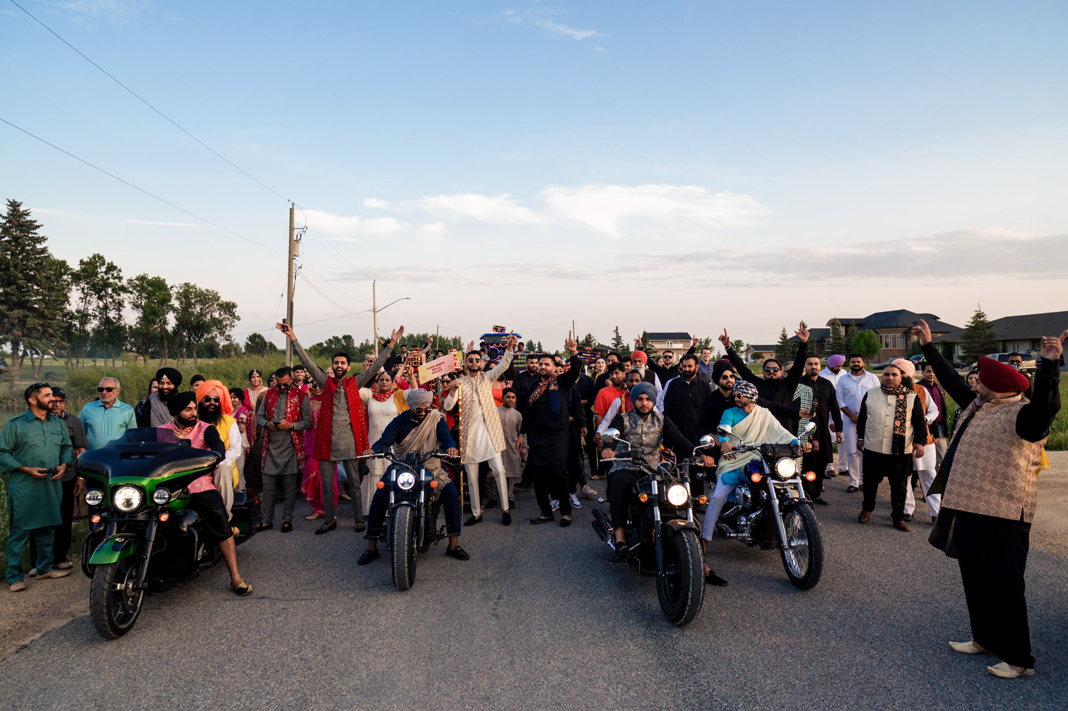A Winnipeg wedding party celebrates on a street with motorcycles under a clear sky.