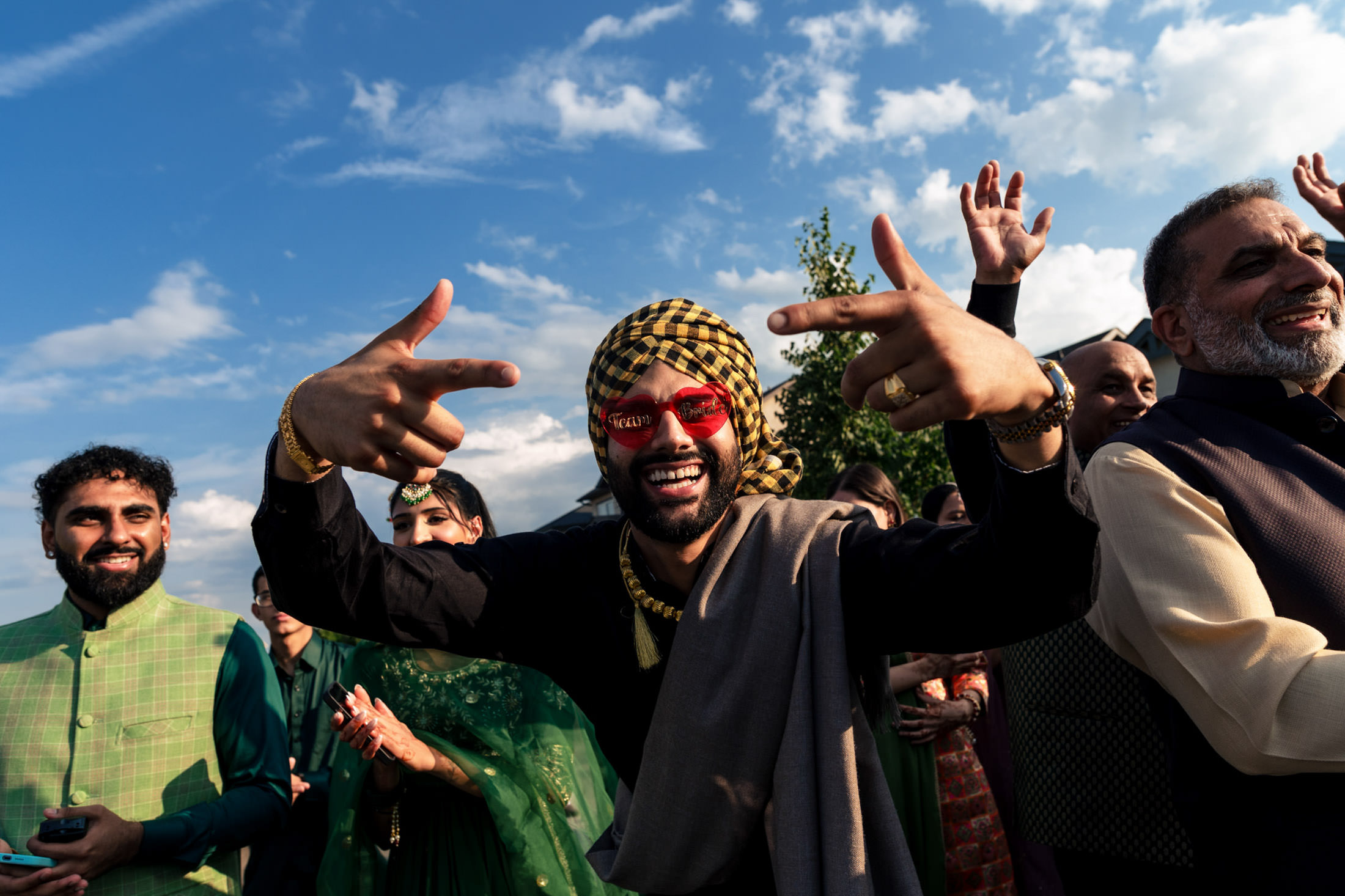 Man in colorful outfit celebrating with a joyful crowd at a Winnipeg wedding under a blue sky.