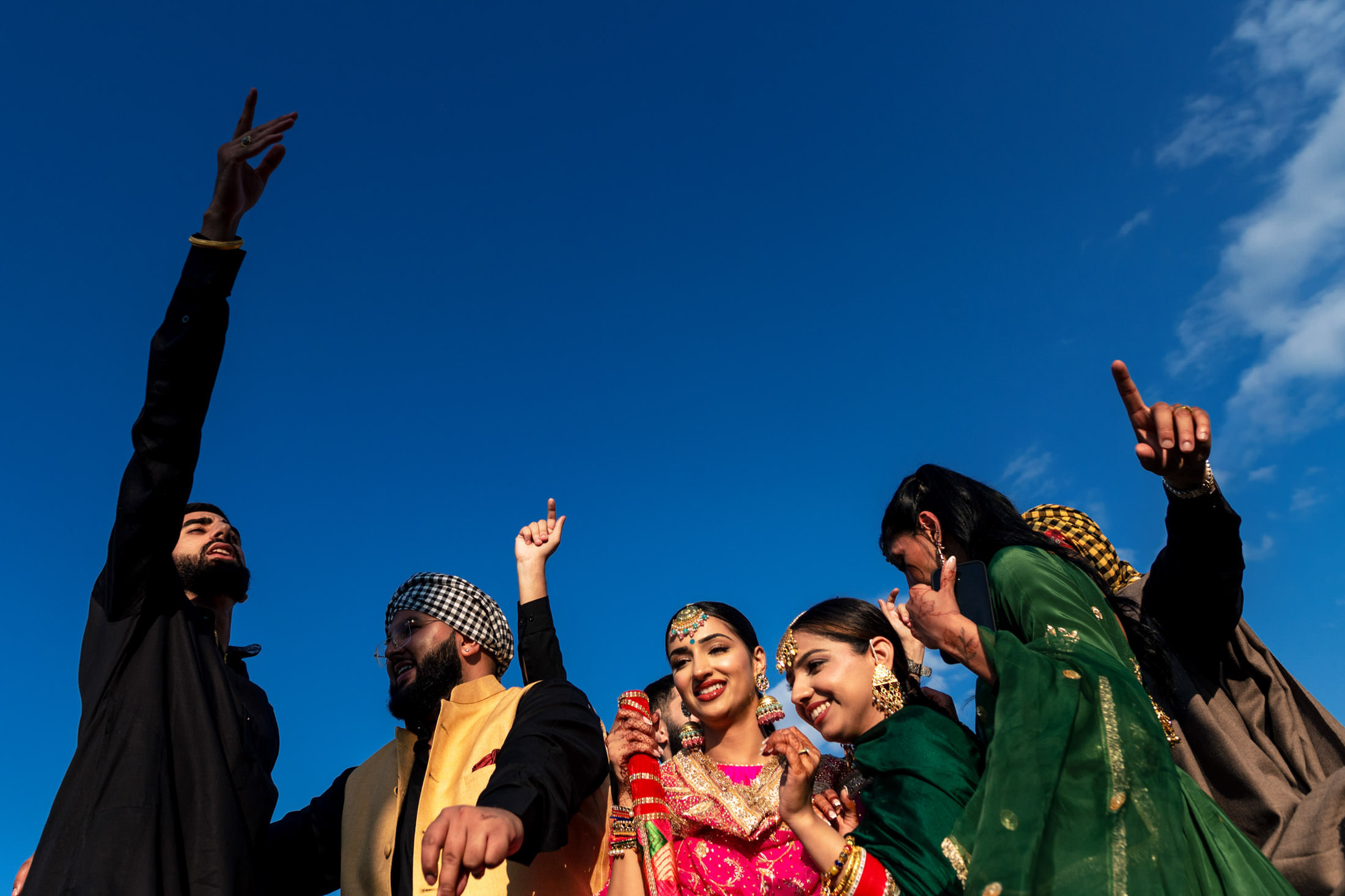 Group of people in colorful attire celebrating a Winnipeg wedding under the clear blue sky.