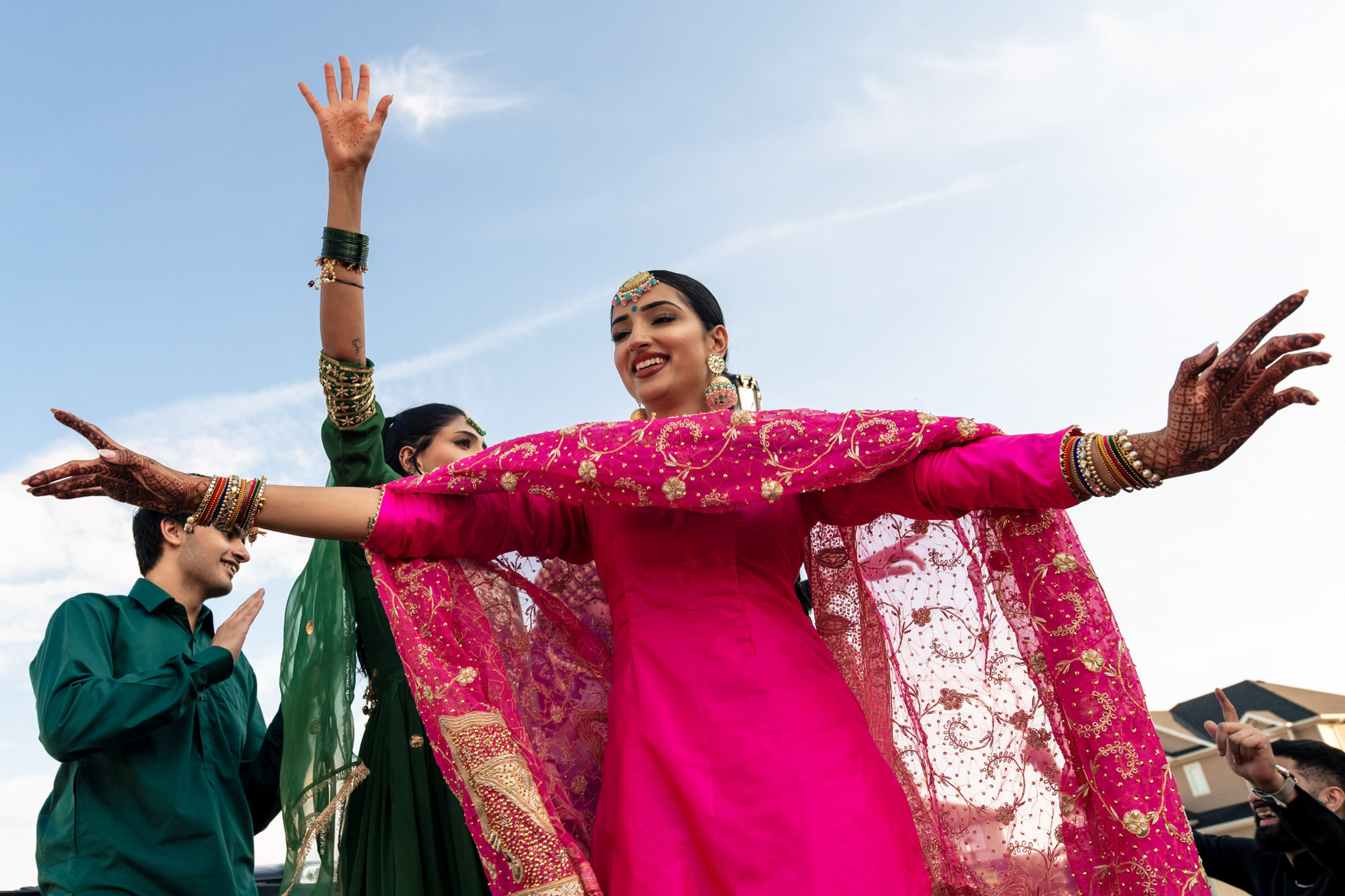 People in colorful attire dancing with joy at a Winnipeg wedding under a bright blue sky.