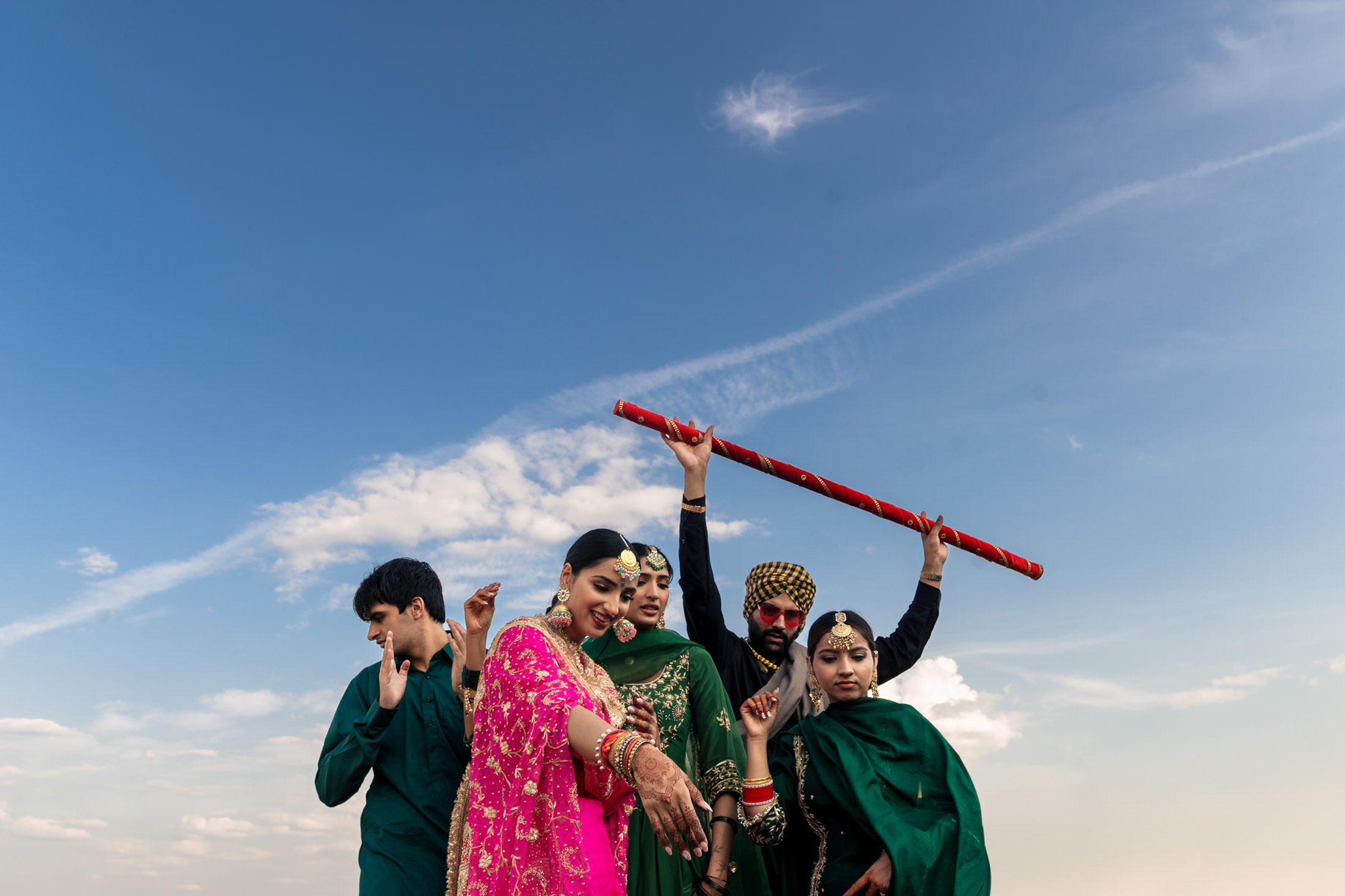 Group of people in colorful traditional attire dancing at a Winnipeg wedding under a cloudy sky.