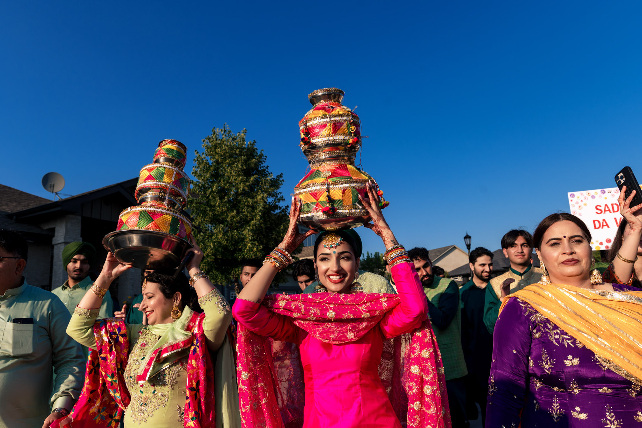 Women in colorful outfits carrying decorated pots at a Winnipeg wedding celebration.