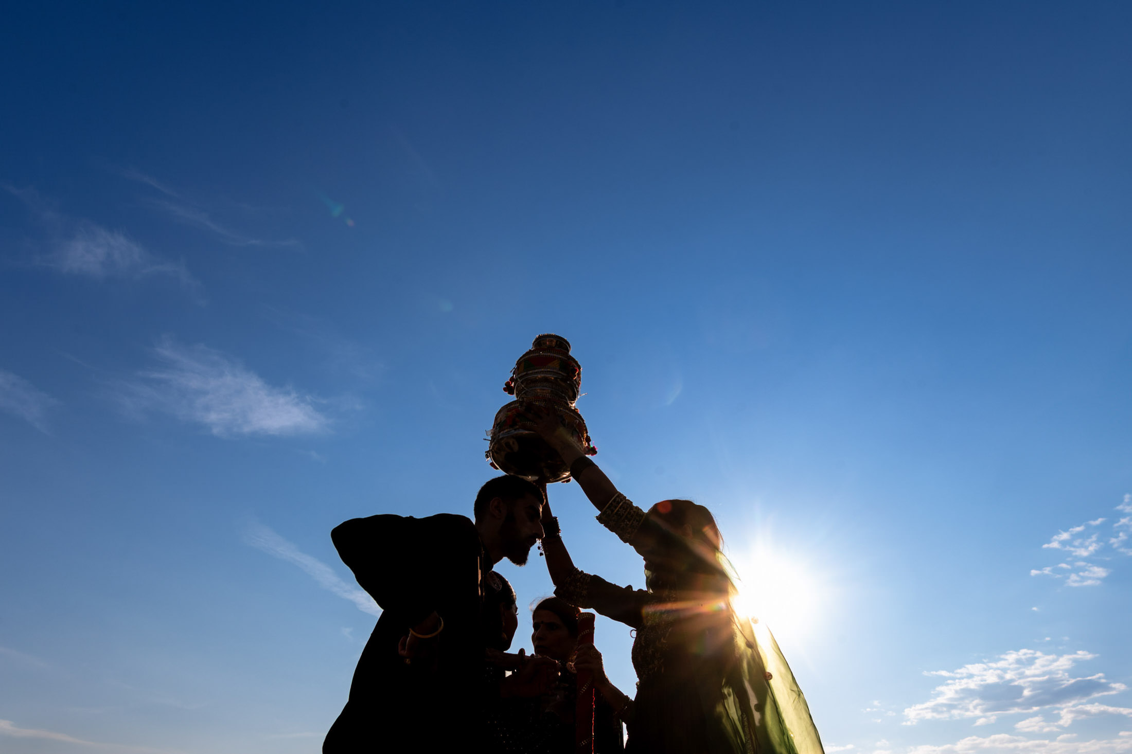 Silhouette of people celebrating a Winnipeg wedding under a bright blue sky with the sun shining.
