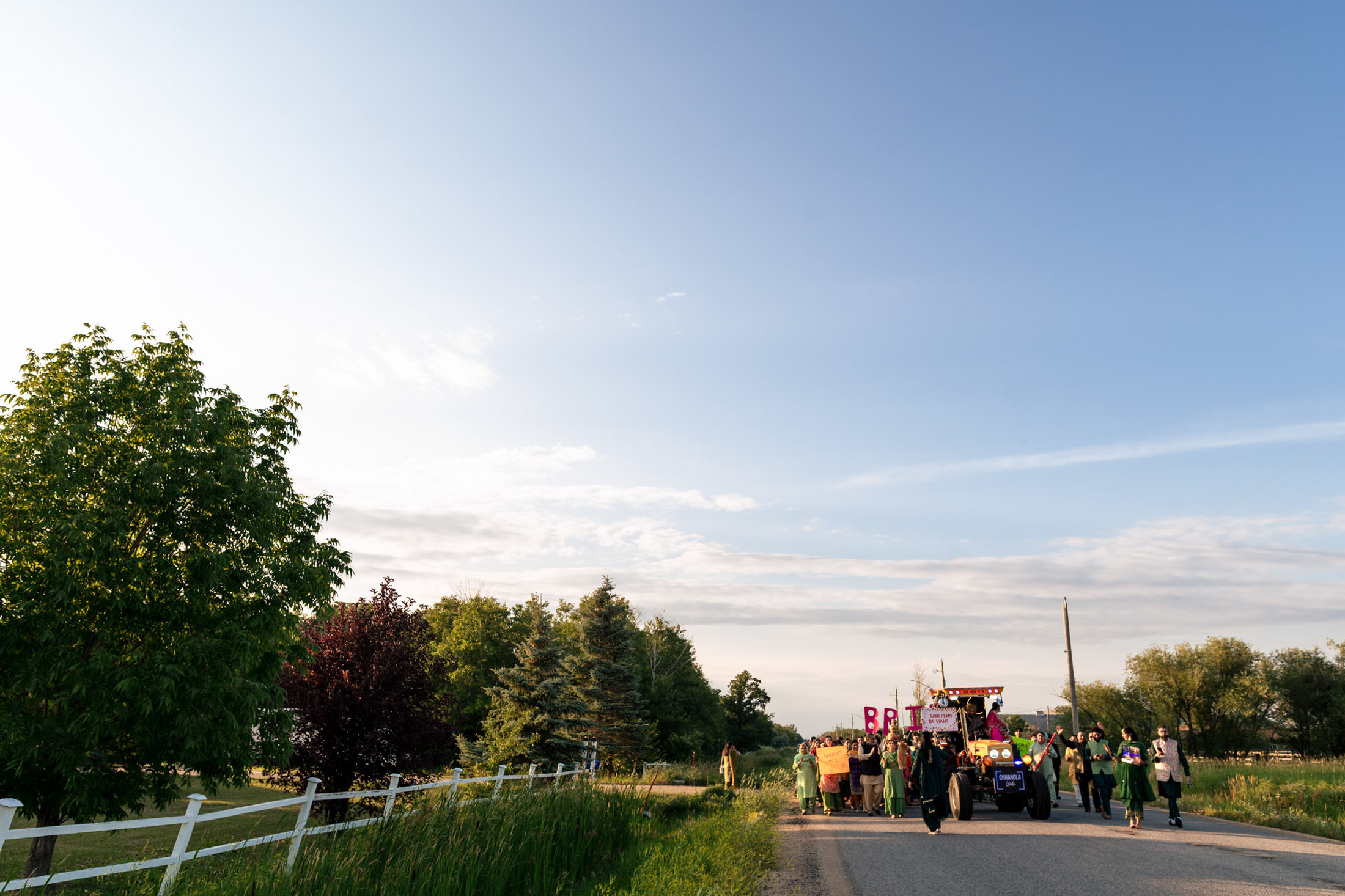 Winnipeg wedding scene: Tractor parade on a country road with trees and clear sky.