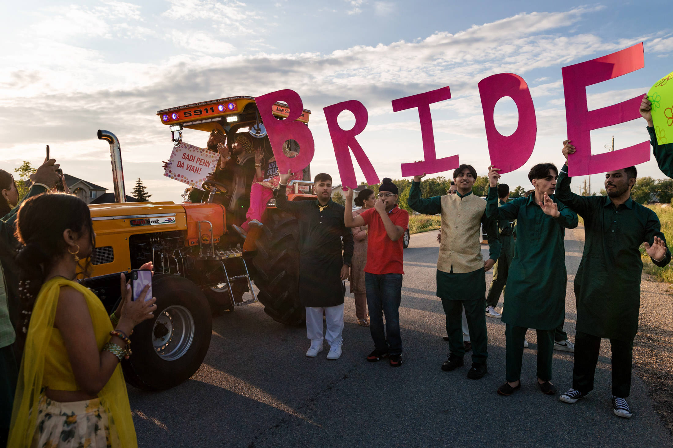 Bride sign held by people near tractor under Winnipeg's sunny wedding sky.