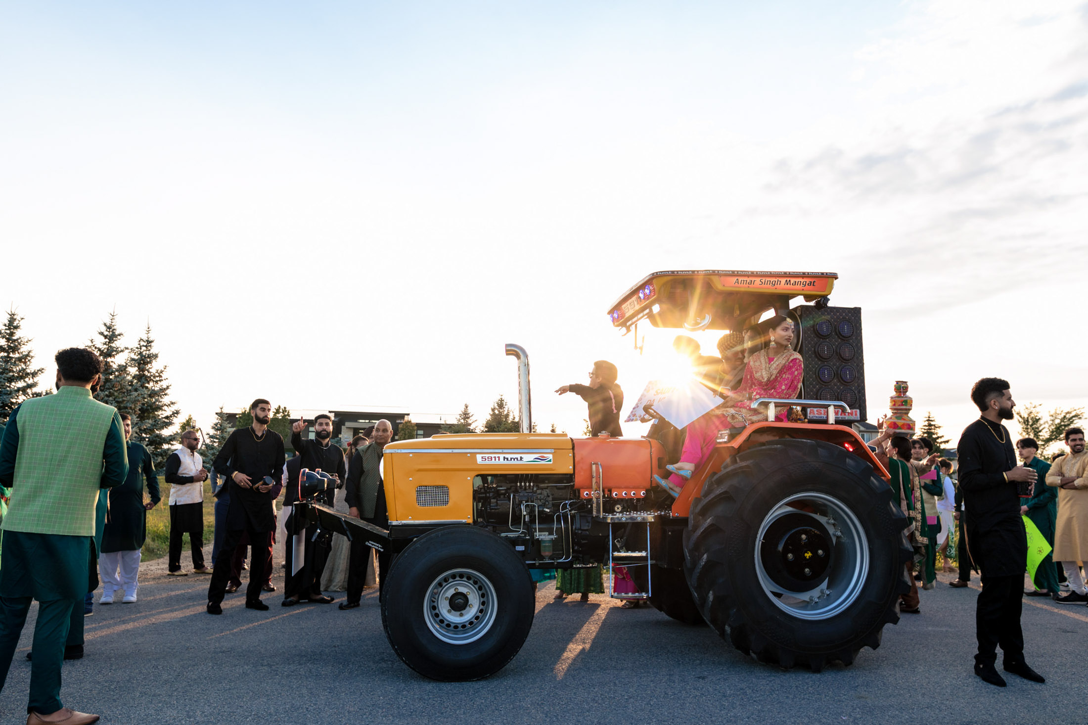 A festive group celebrates around a decorated tractor at a Winnipeg wedding sunset.