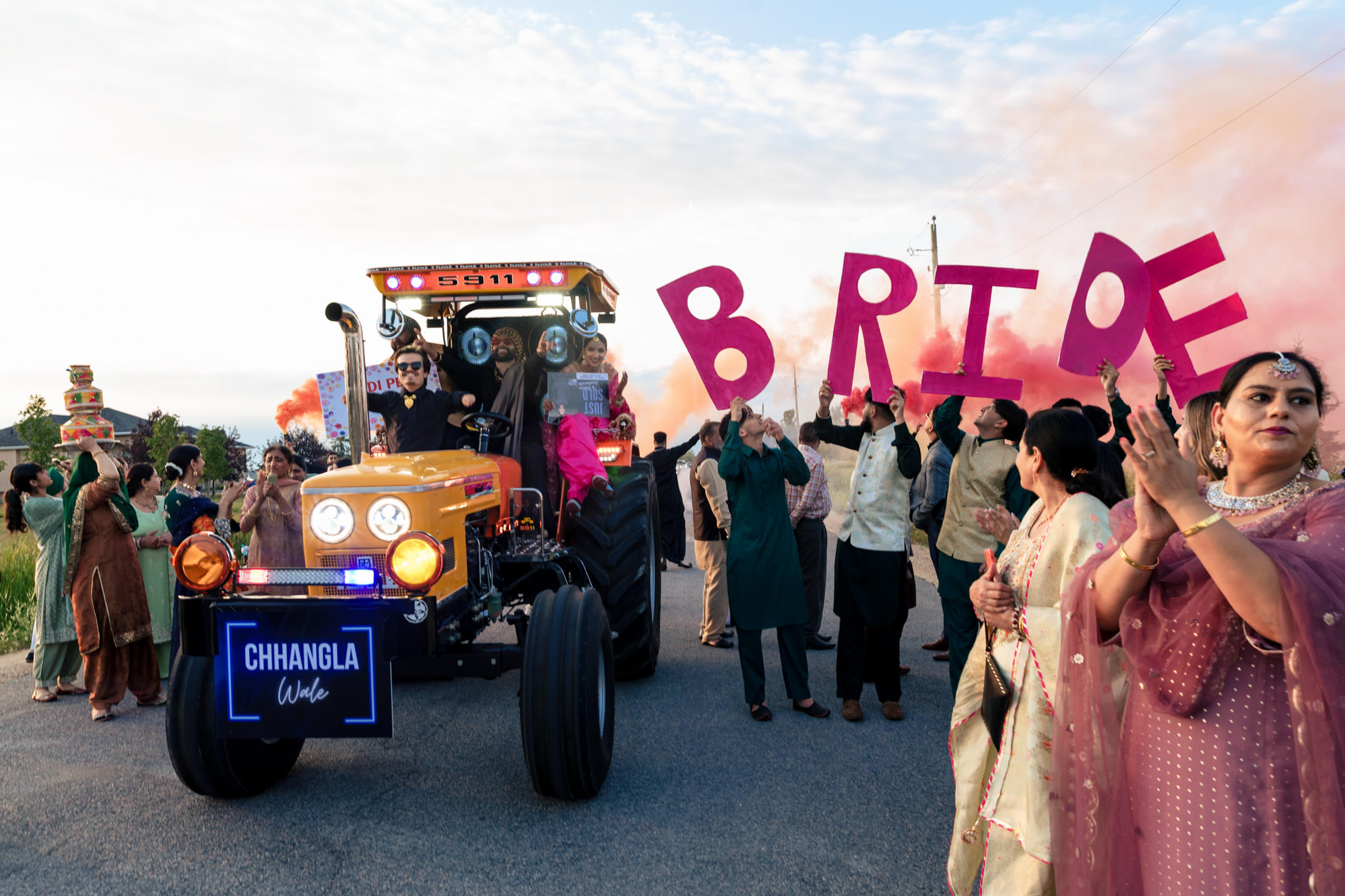 Bride on a tractor at Winnipeg wedding, with "BRIDE" sign and pink smoke in the background.