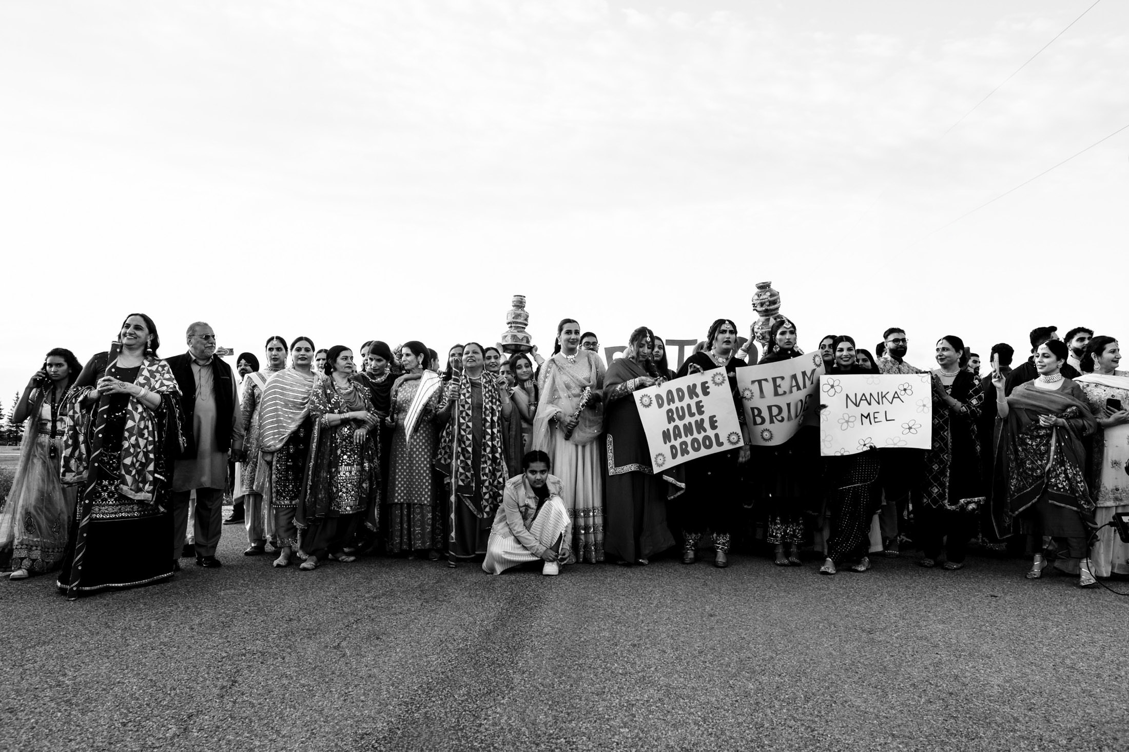 A group in traditional clothing stands on a road, holding signs, celebrating a Winnipeg wedding.
