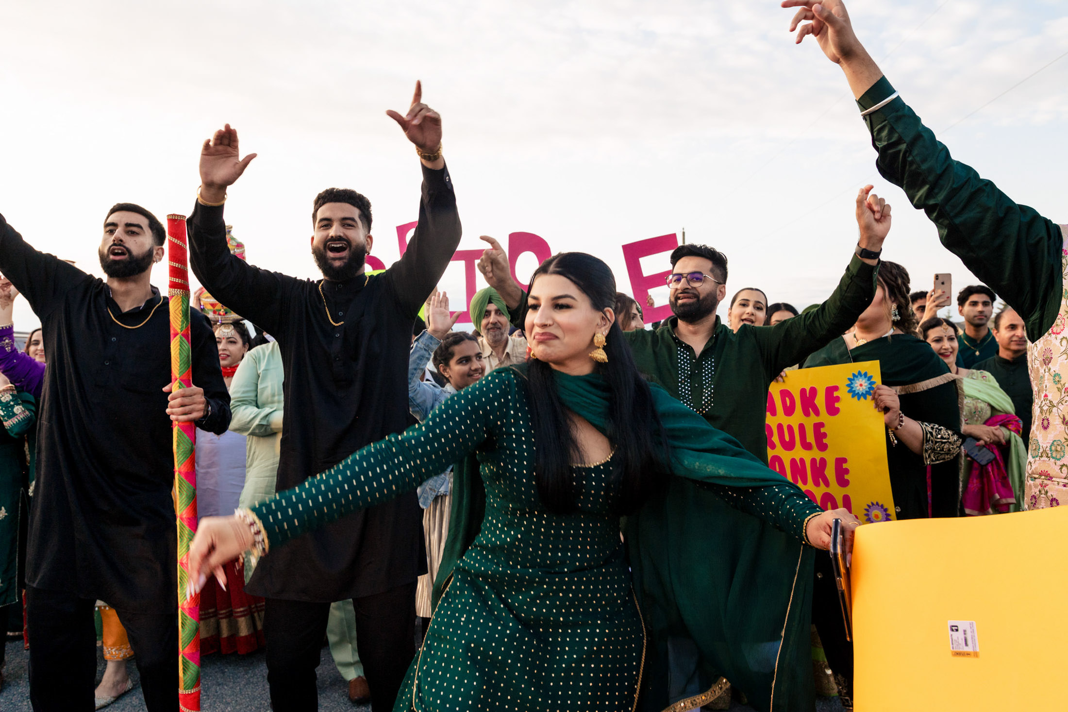 People joyfully dance outdoors at a Winnipeg wedding, wearing vibrant traditional clothing.
