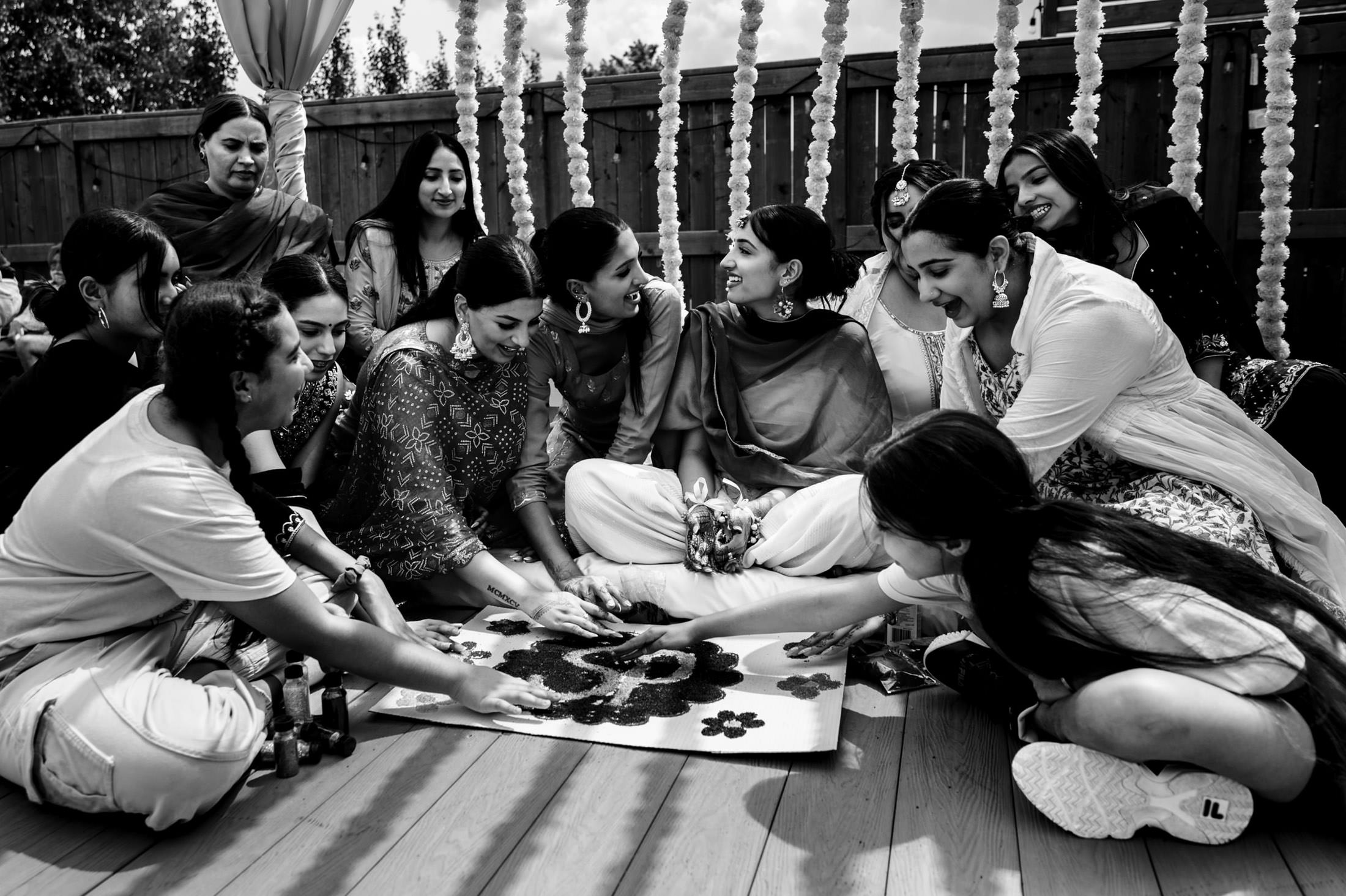 Group of people joyfully creating rangoli art together at a festive Winnipeg wedding.