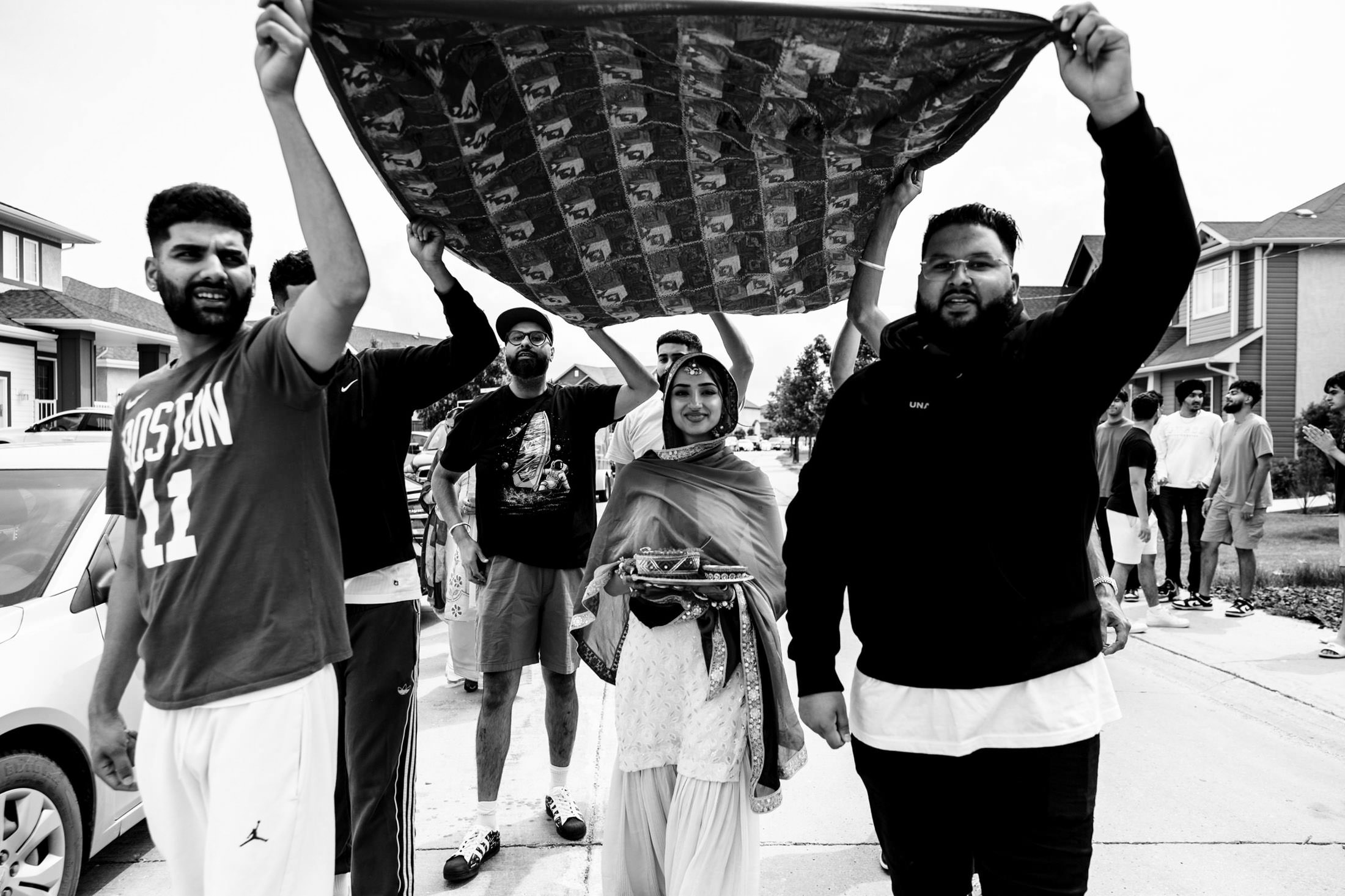 Group at a Winnipeg wedding, two holding a canopy, one carrying an item. Black and white.