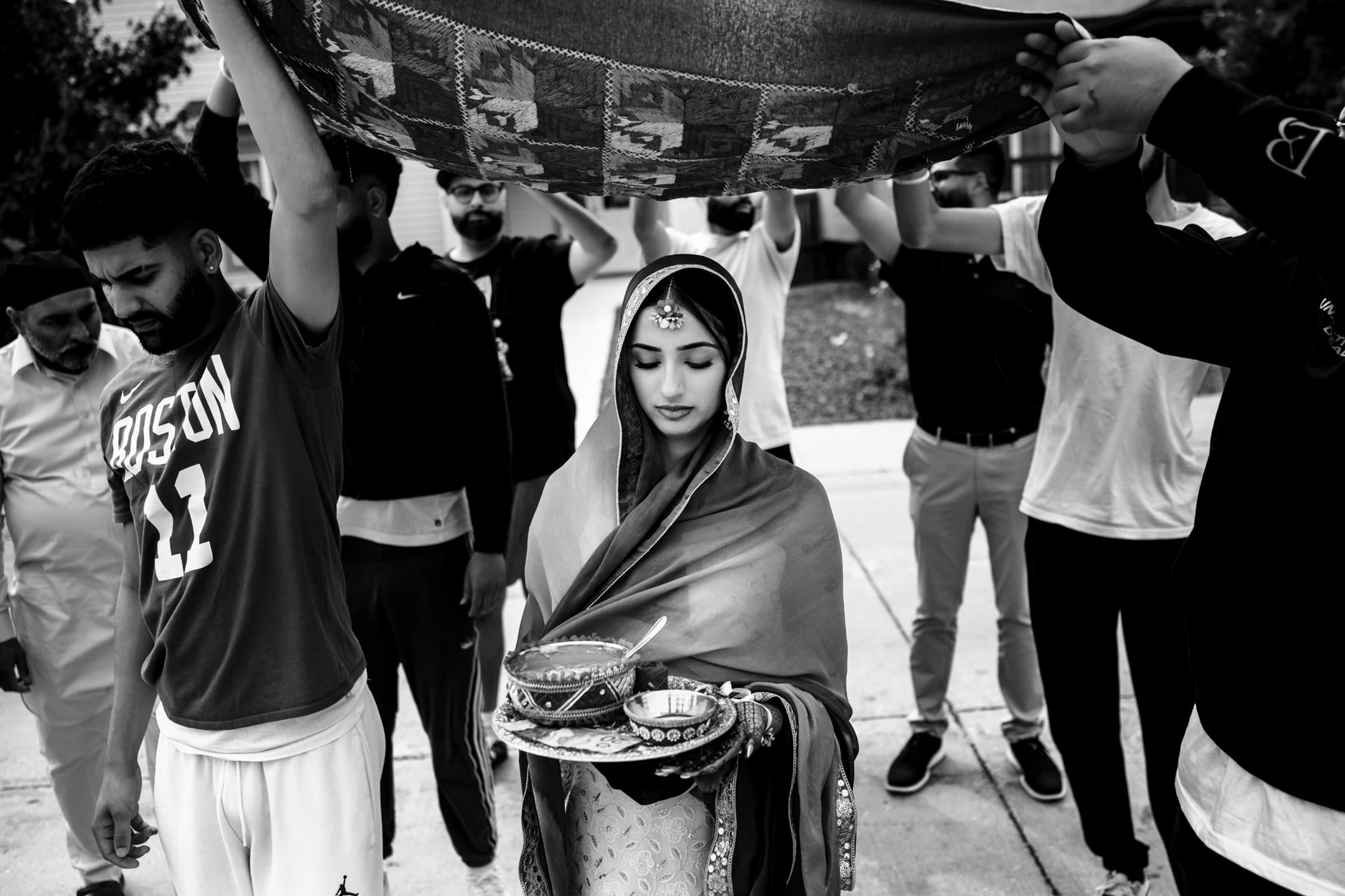 Bride holds ceremonial items under canopy, surrounded by guests at a Winnipeg wedding ritual.