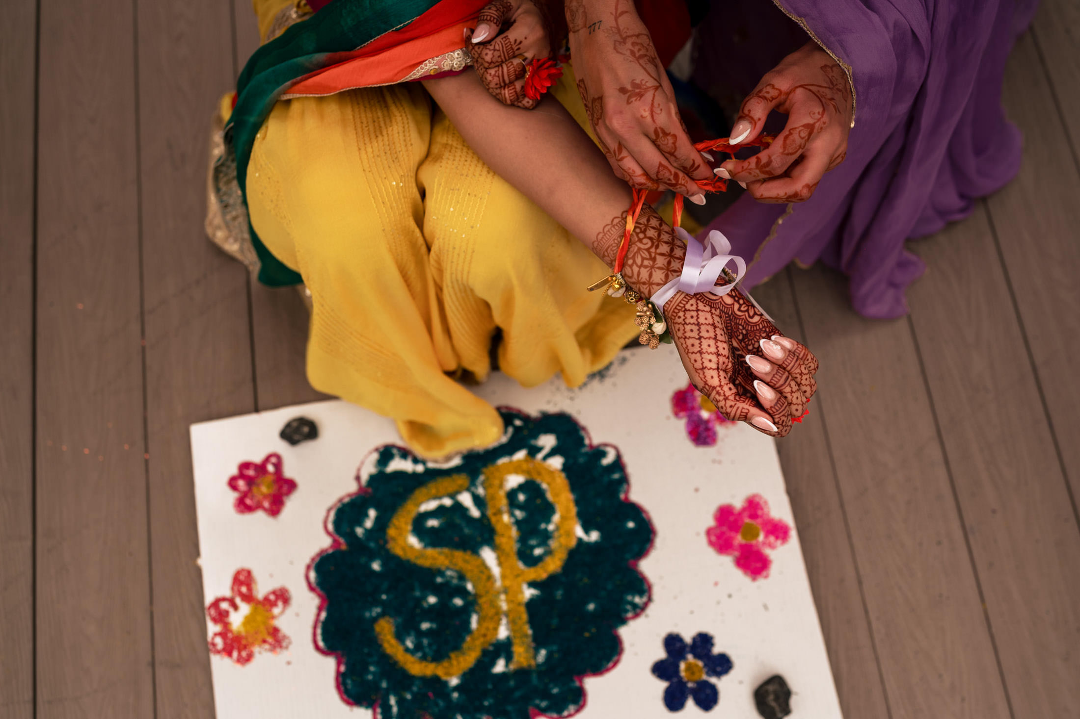 Hands tying rakhi, floral designs, "SP" in sand; a Winnipeg wedding touch.