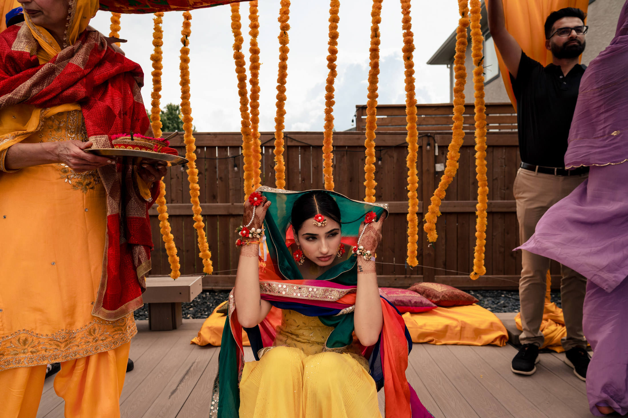 Woman in colorful attire seated under marigold strings at a Winnipeg wedding ceremony.