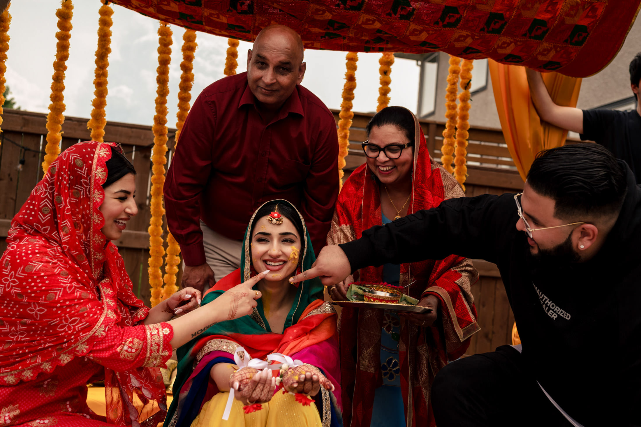 Smiling bride in a colorful Winnipeg wedding, surrounded by family and marigold garlands.