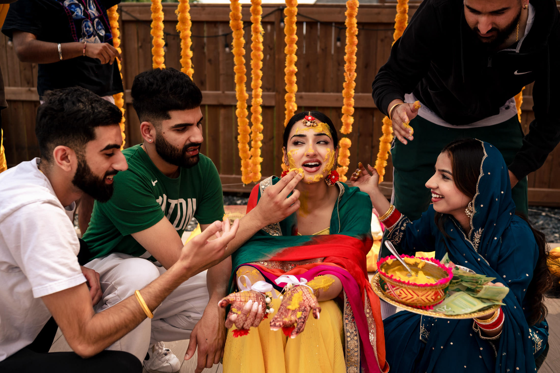 At a Winnipeg wedding, people celebrate by applying turmeric paste to a smiling woman.