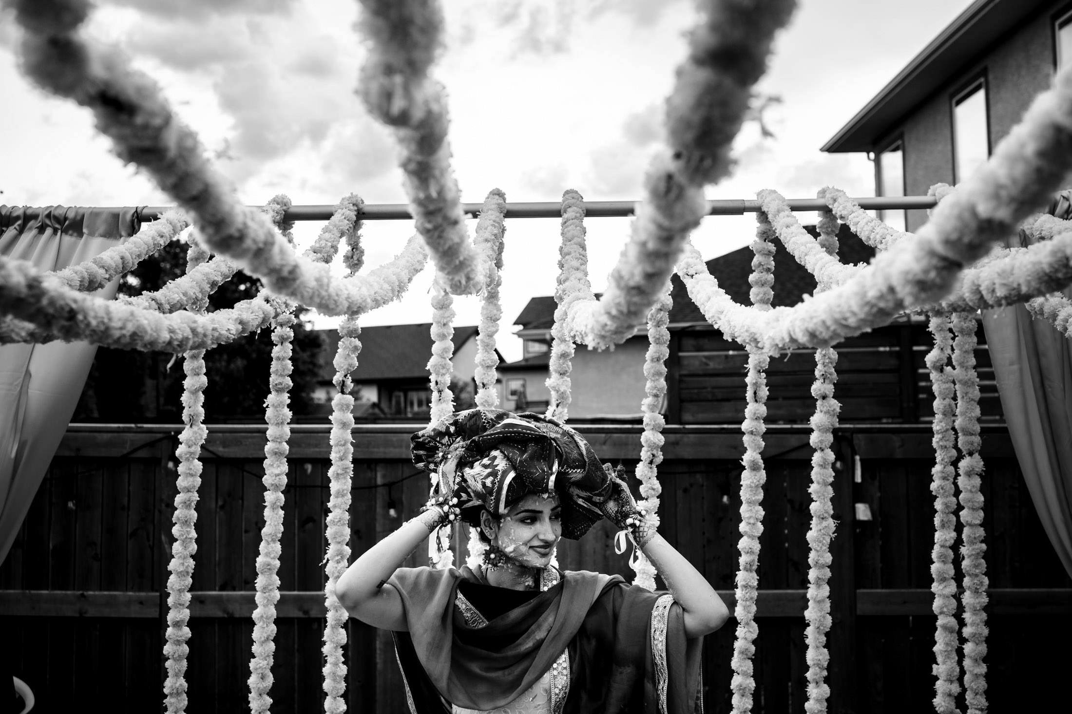 Bride adjusts headpiece under garland, captured in black and white at a Winnipeg wedding.