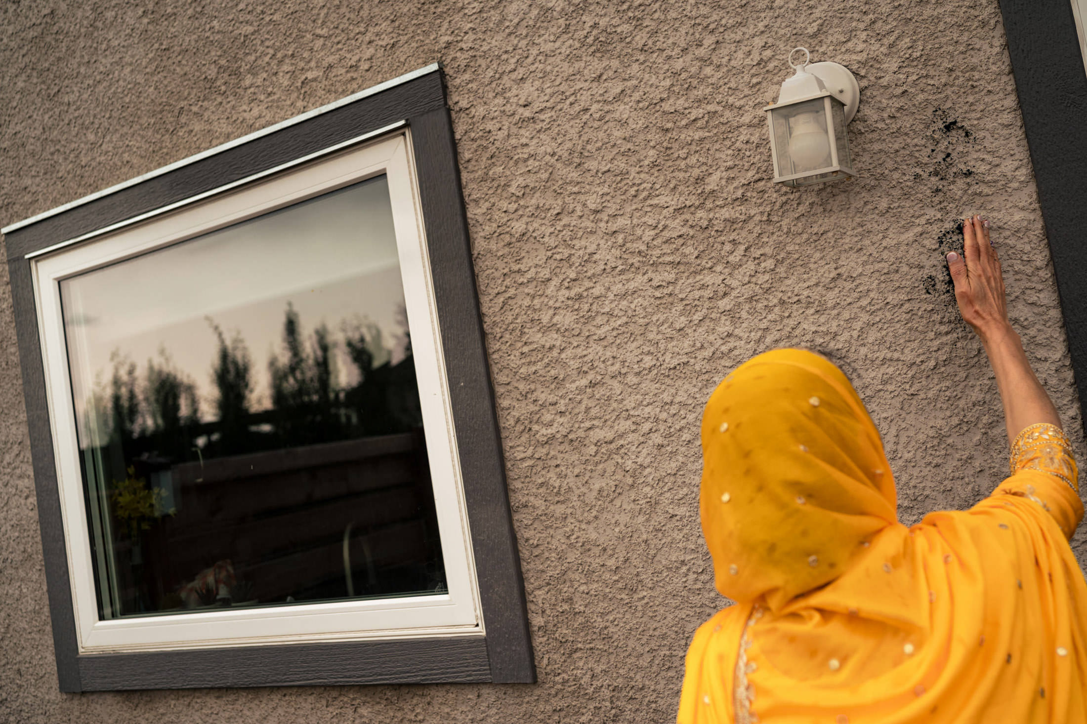 Person in yellow headscarf touches house wall near window and light, dreaming of Winnipeg wedding.