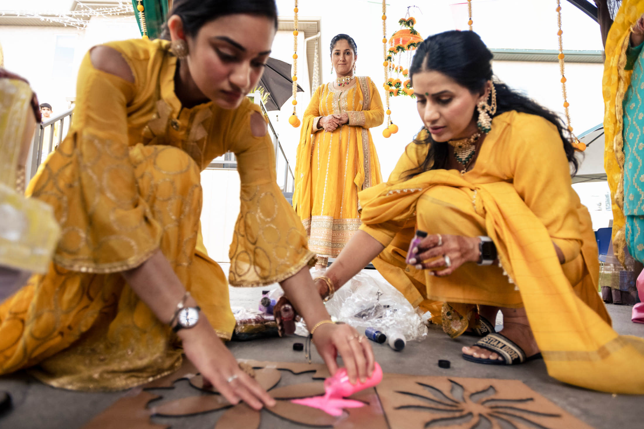Women in yellow outfits decorating with stencils and paint for a Winnipeg wedding celebration.