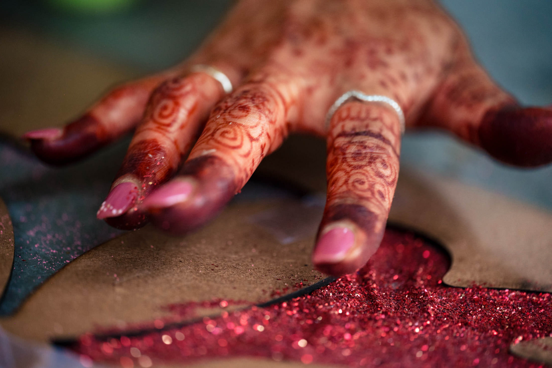 Winnipeg wedding vibes: Hand with henna and pink nails touching red glitter.