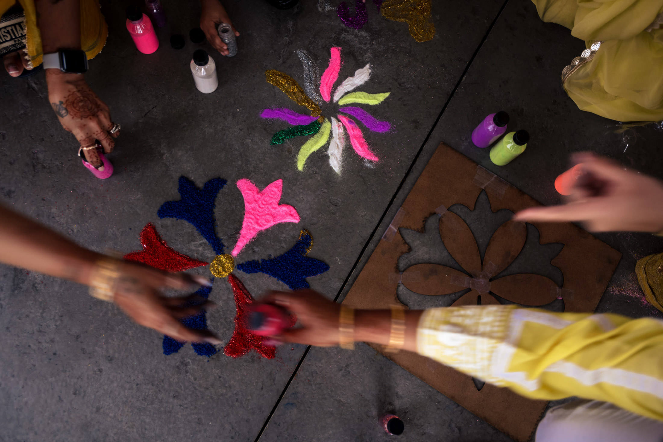 Hands decorating a rangoli for a vibrant Winnipeg wedding with colorful powders and stencils.