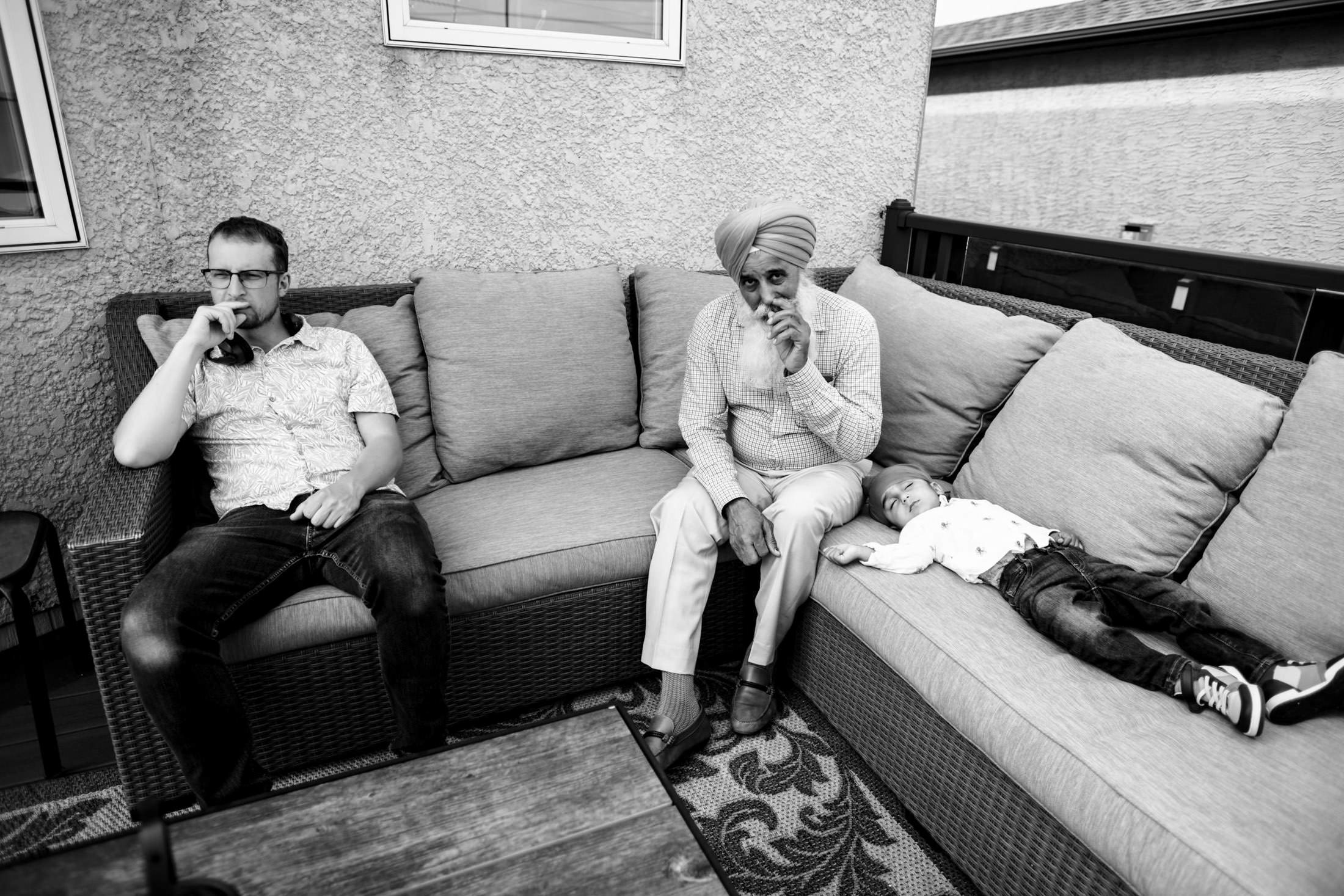 Three people relaxing on a patio sofa; one is sleeping, two are seated, pondering a Winnipeg wedding.