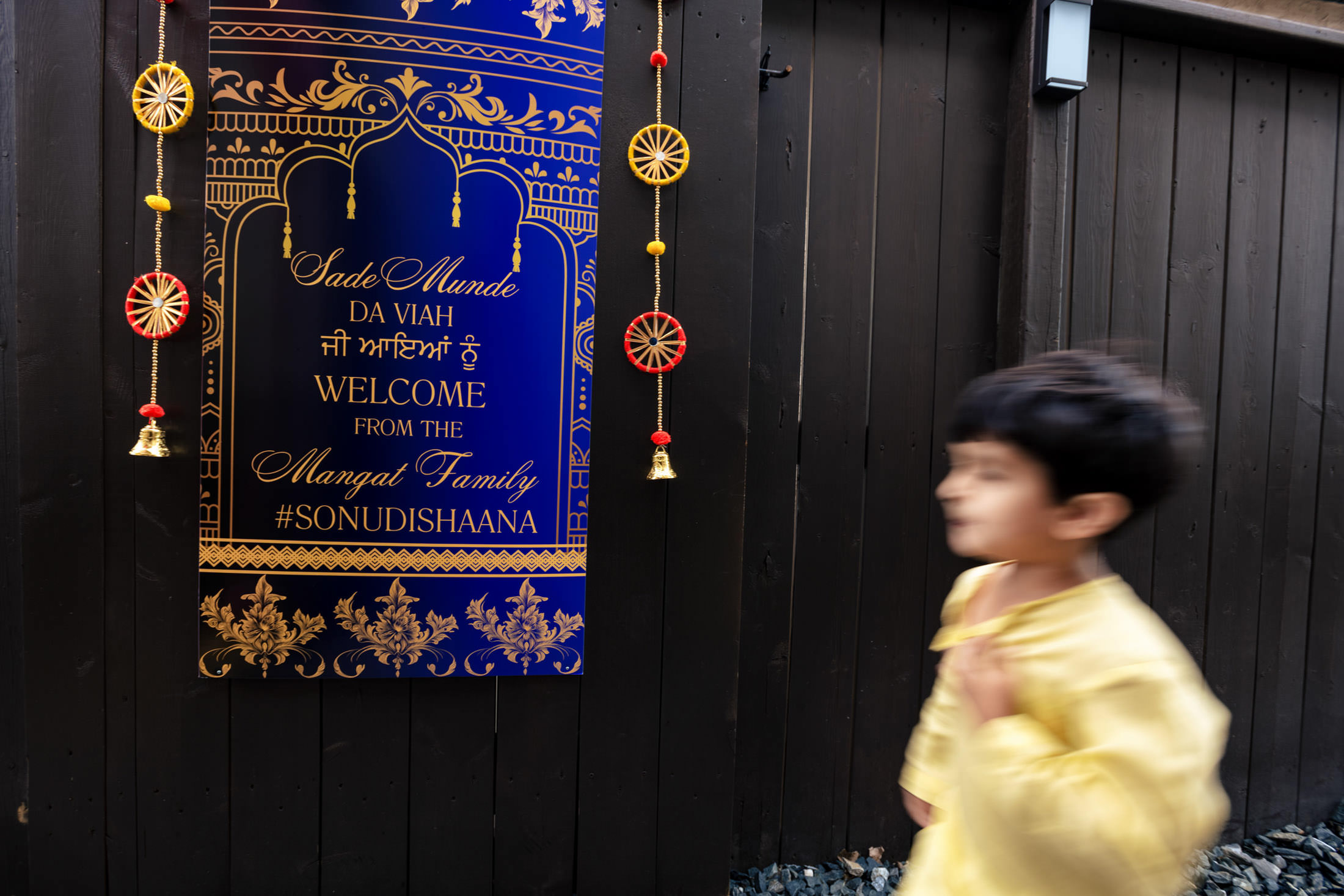 A blurred child in yellow walks by a decorative welcome sign at a Winnipeg wedding.