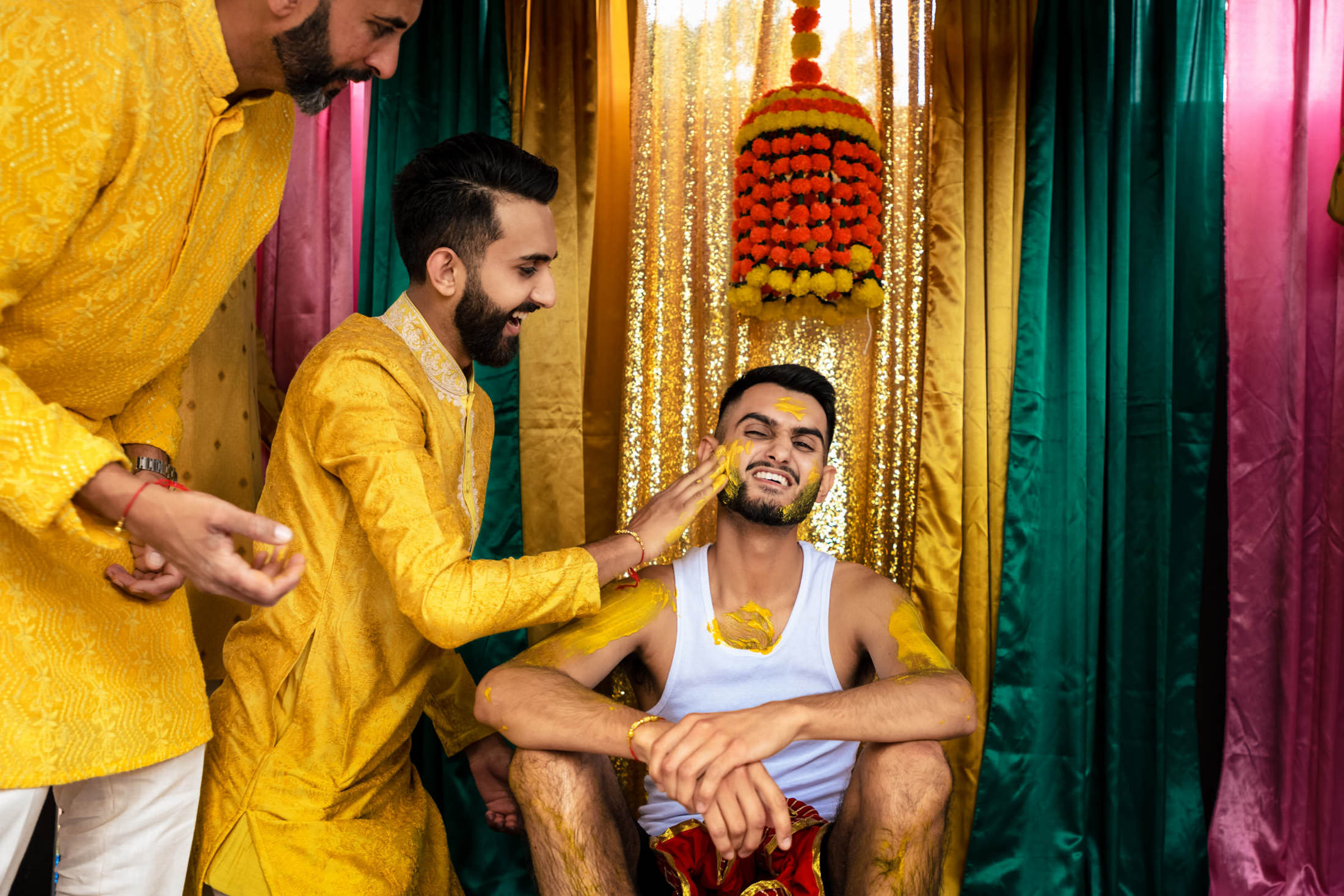 Man in traditional attire applies turmeric to another man at a Winnipeg wedding celebration.