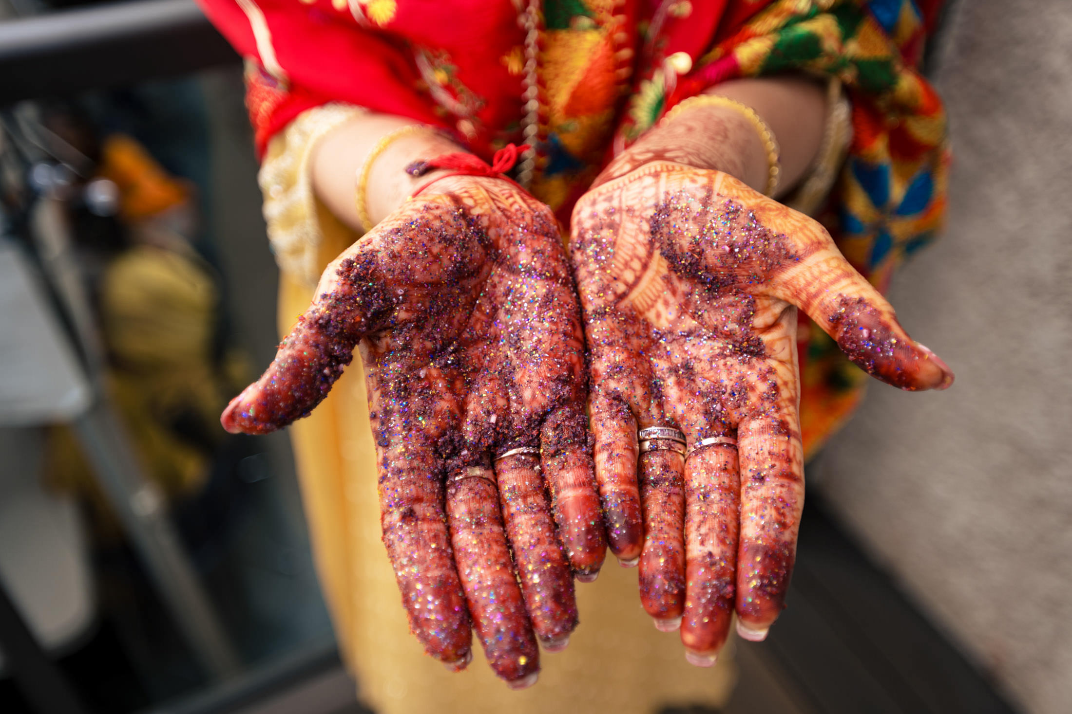 Hands with intricate henna and glitter, wearing vibrant attire at a Winnipeg wedding.