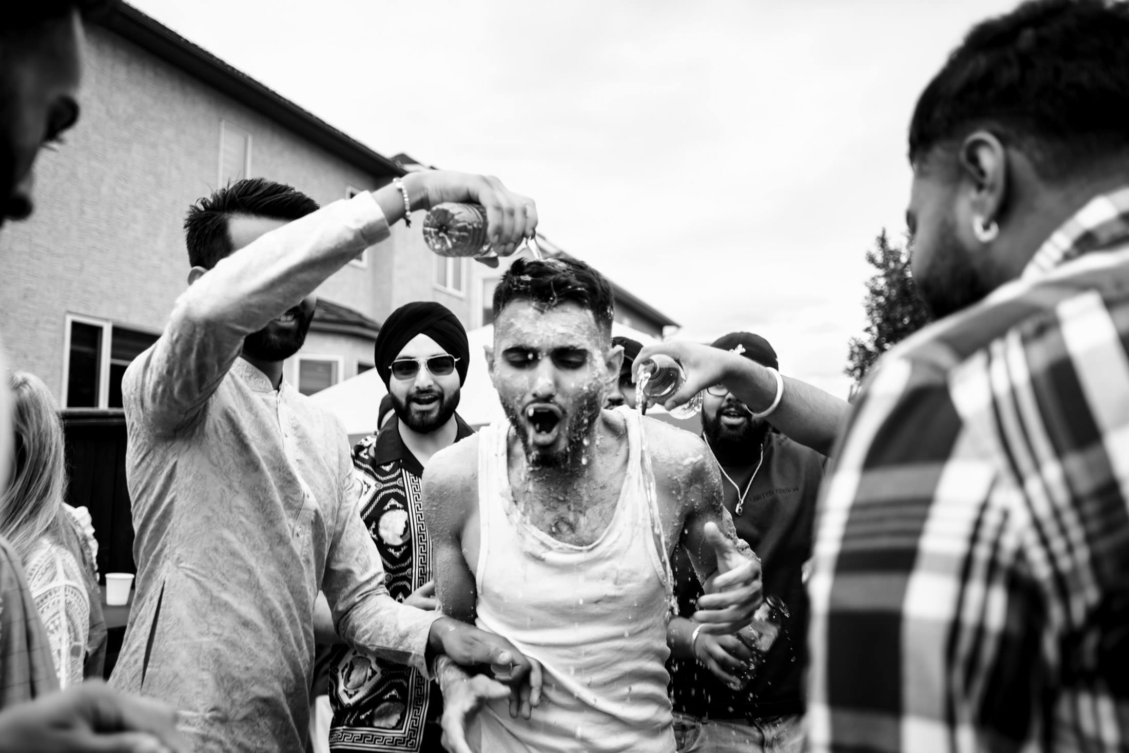 Group of men at a Winnipeg wedding pouring liquid on a laughing man; festive atmosphere.