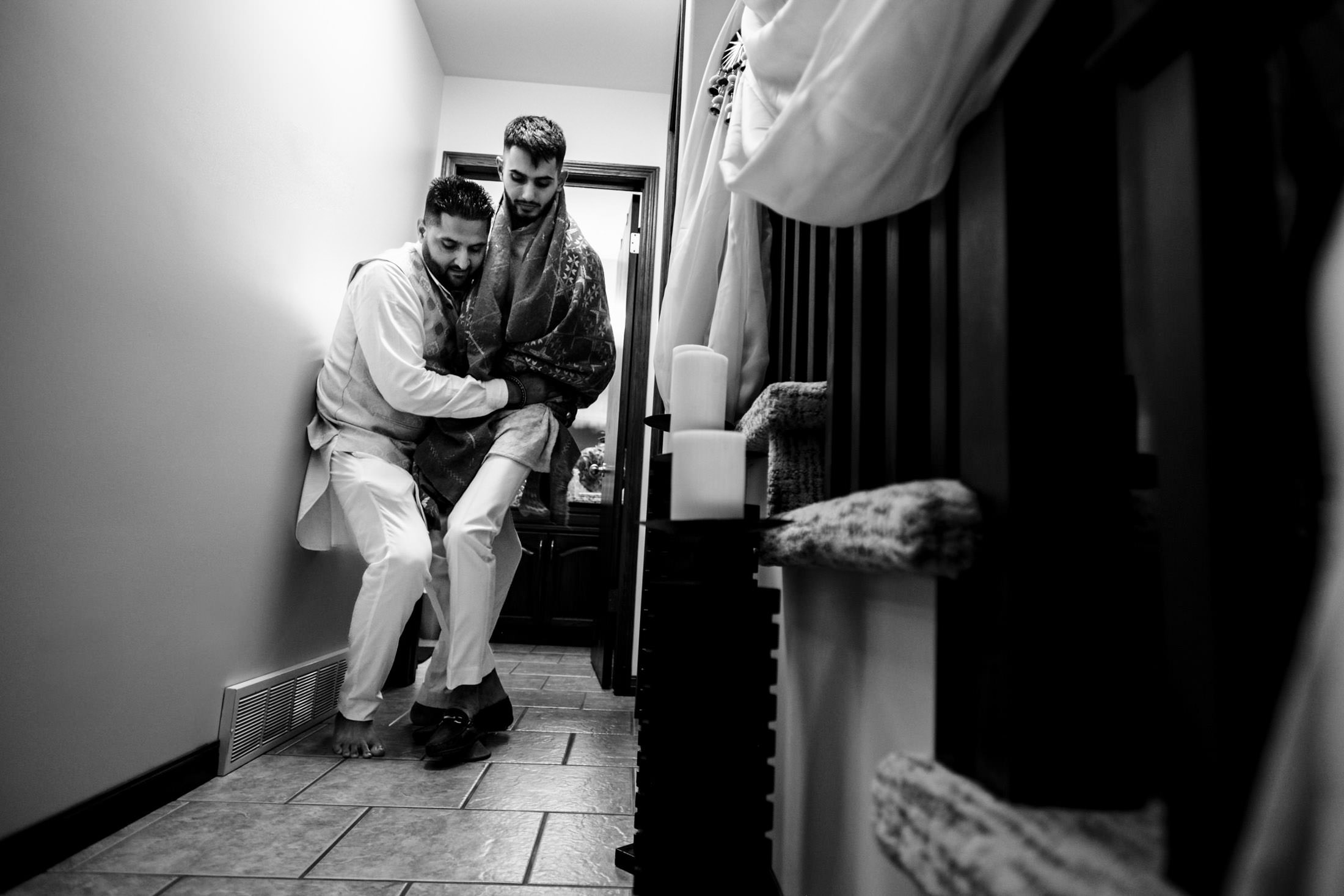 Two men laughing and hugging in a narrow hallway, one wrapped in a Winnipeg wedding blanket.