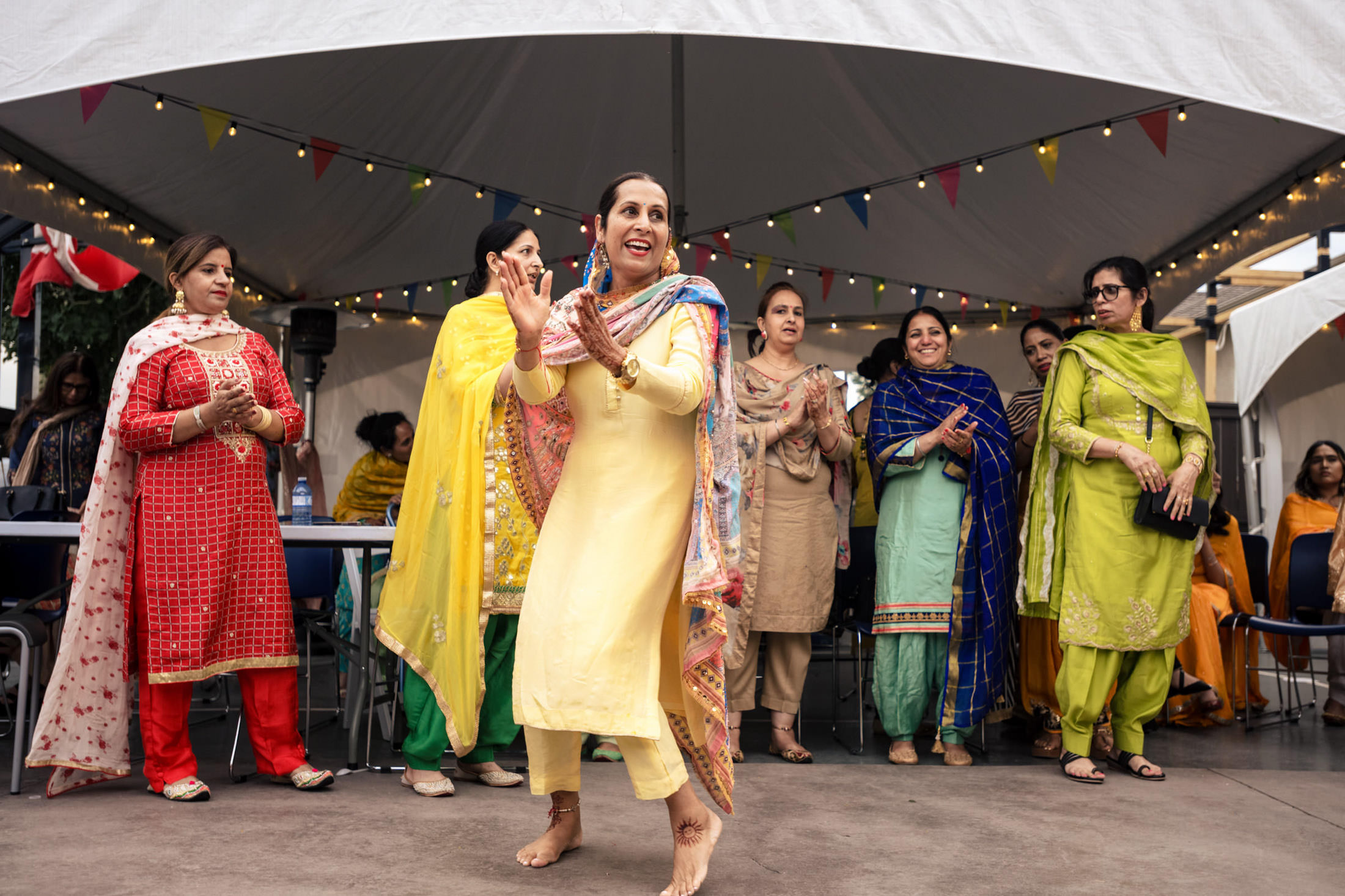 Woman in yellow dancing joyfully at a Winnipeg wedding, others clapping under a tent.