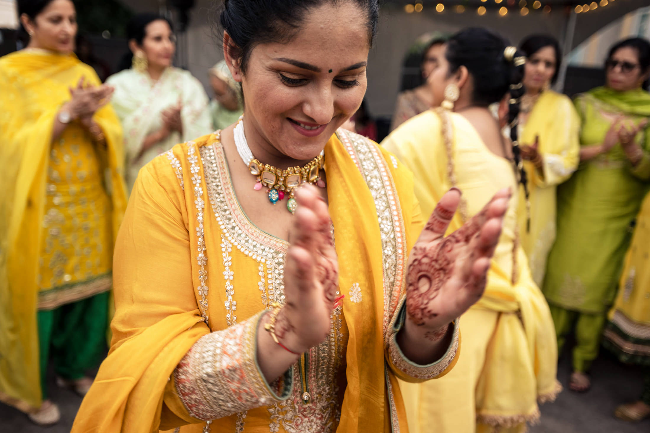 Woman in yellow traditional attire clapping at a joyous Winnipeg wedding celebration.
