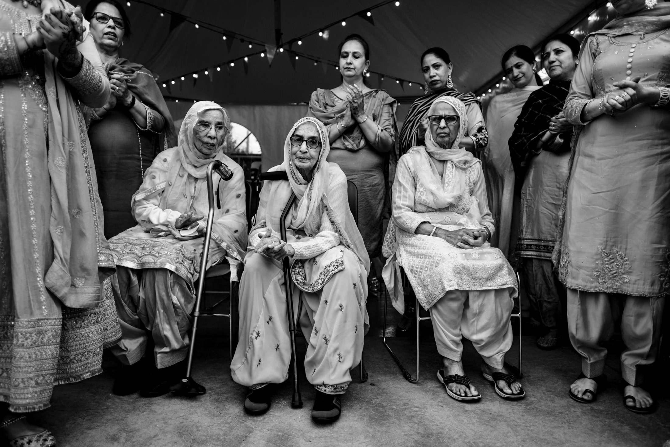 Elderly women enjoy a Winnipeg wedding, seated together under a tent amidst the gathering.