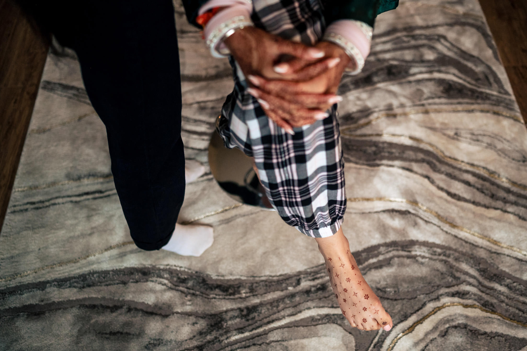 Two people sit on a patterned rug; one in plaid pants and star socks at a Winnipeg wedding.
