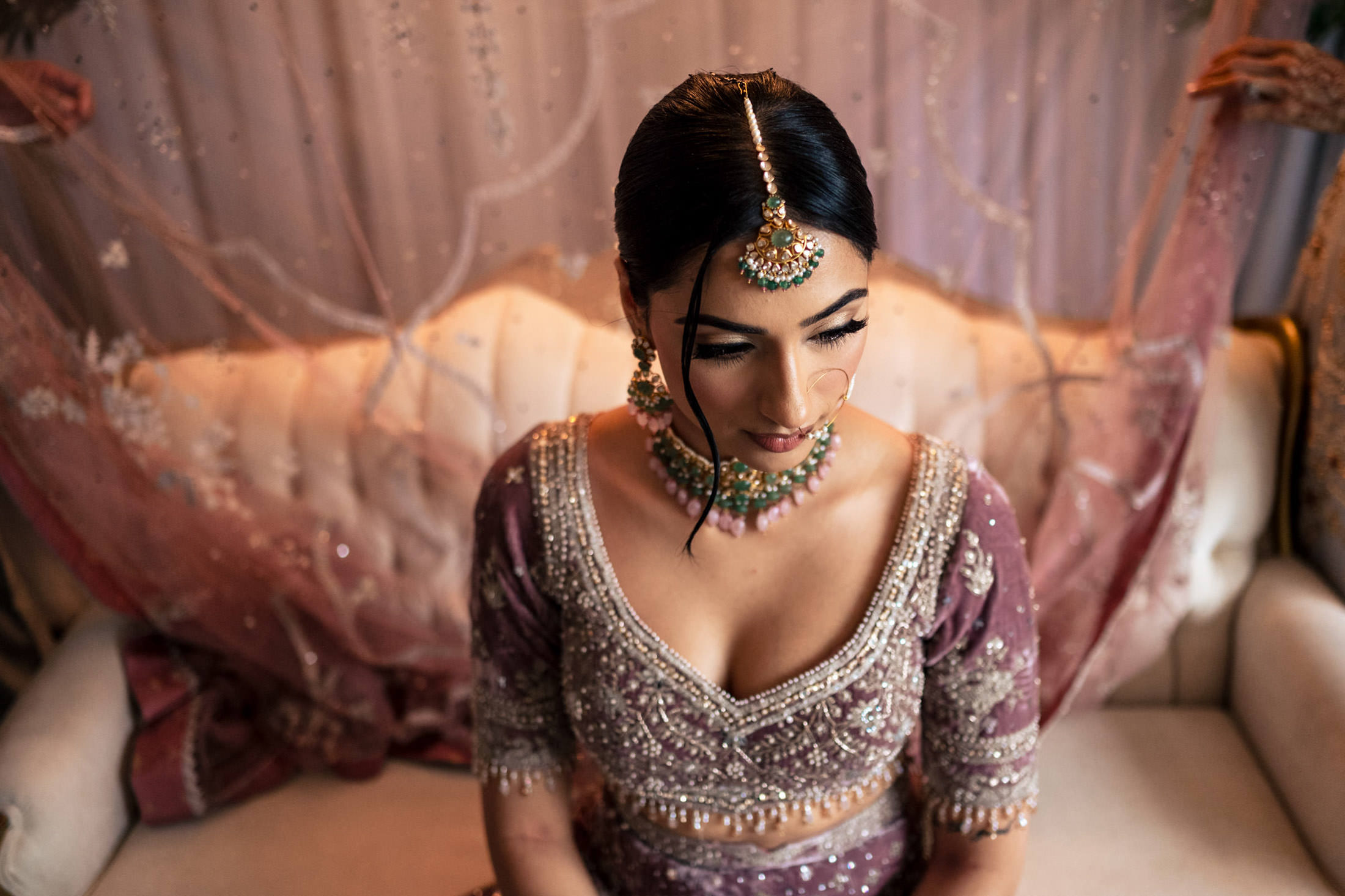 Bride in ornate lavender attire and jewelry, seated on a white sofa at a Winnipeg wedding.