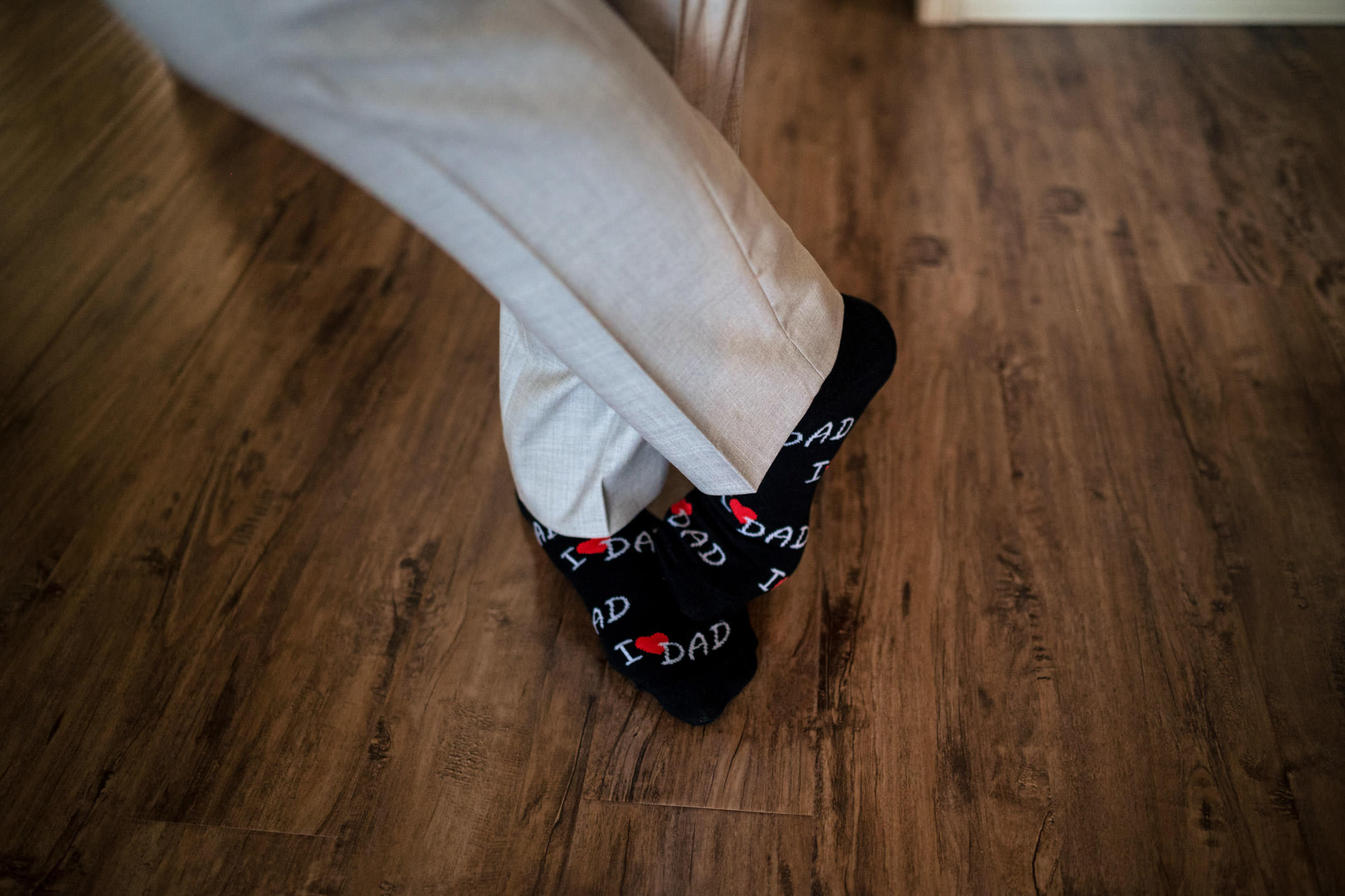 Person in "I ♥ Dad" socks, standing on wooden floor, ready for a Winnipeg wedding.