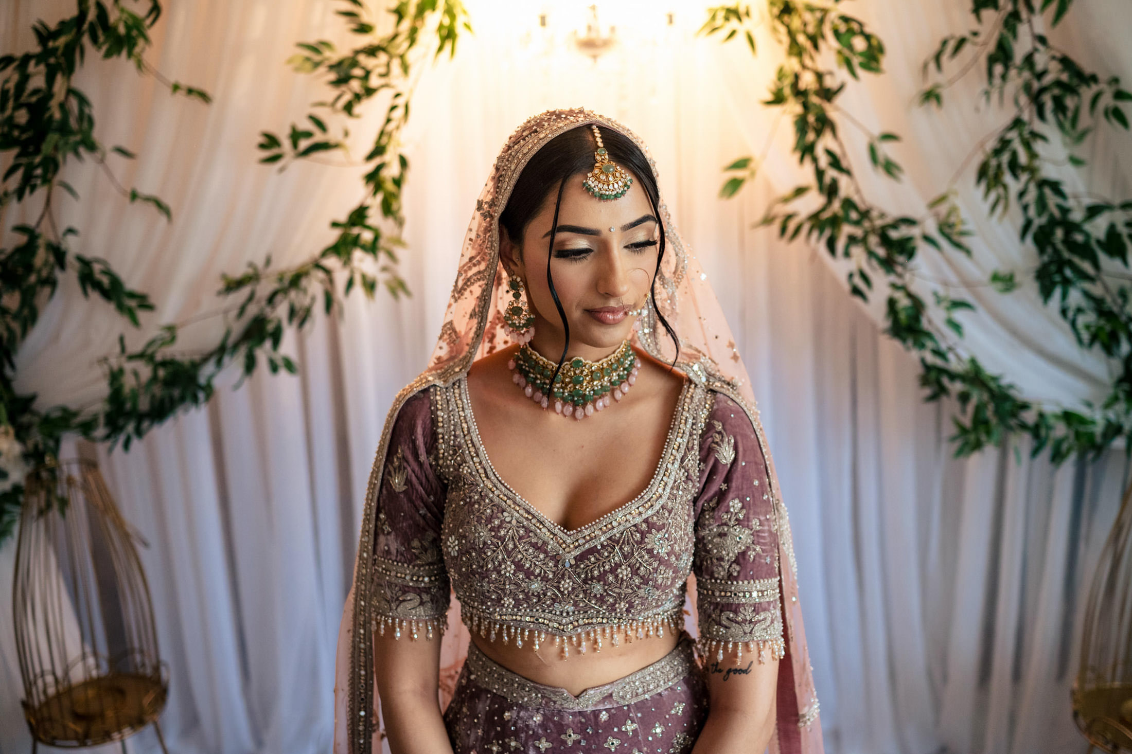 Bride in detailed traditional attire, set against lush greenery at a Winnipeg wedding.